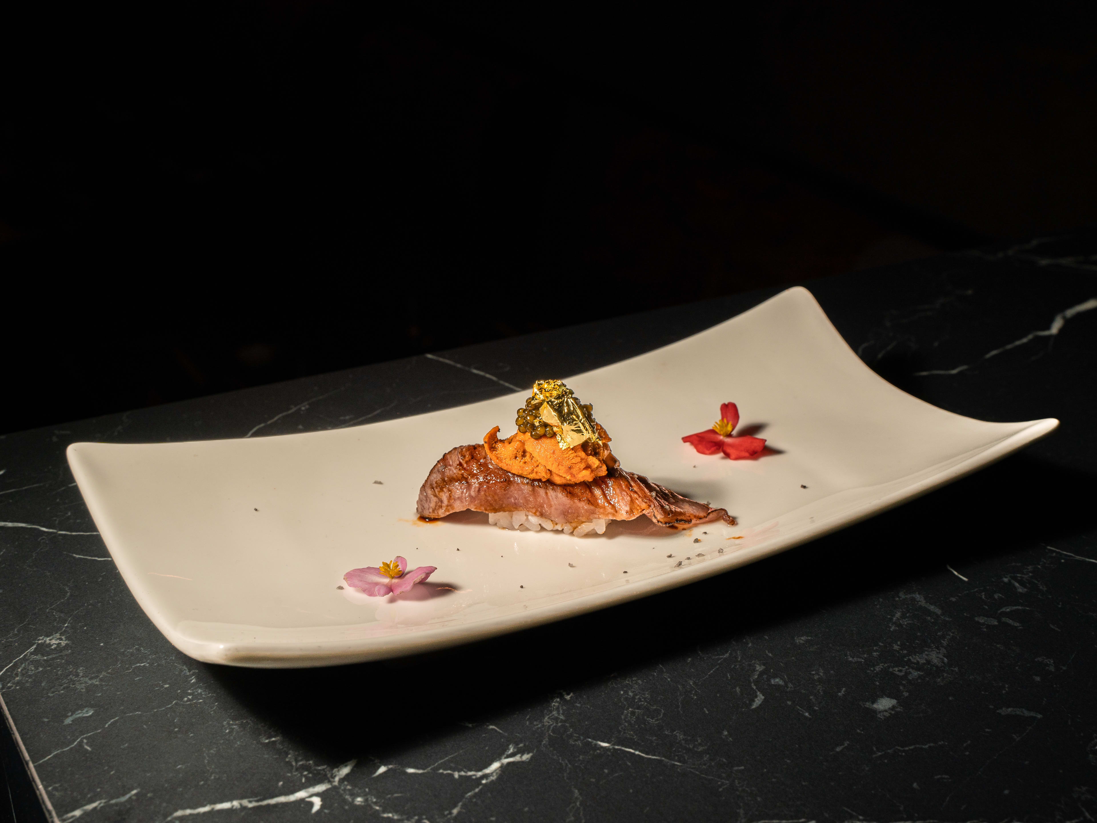 rectangular plate with a single piece of sushi topped with fish, uni, and gold leaf