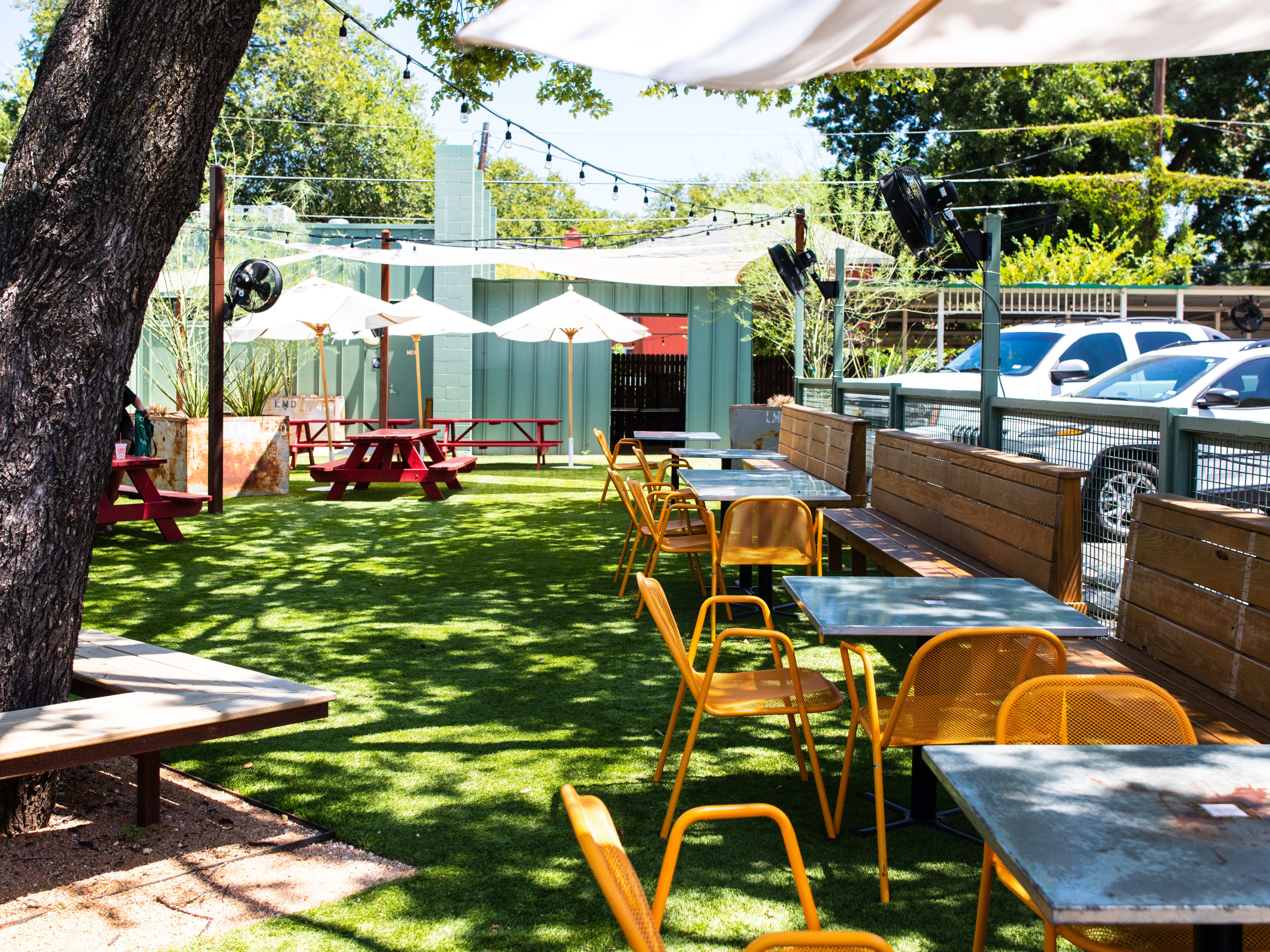 The backyard at Lou's shaded by a large tree and umbrellas at picnic tables.