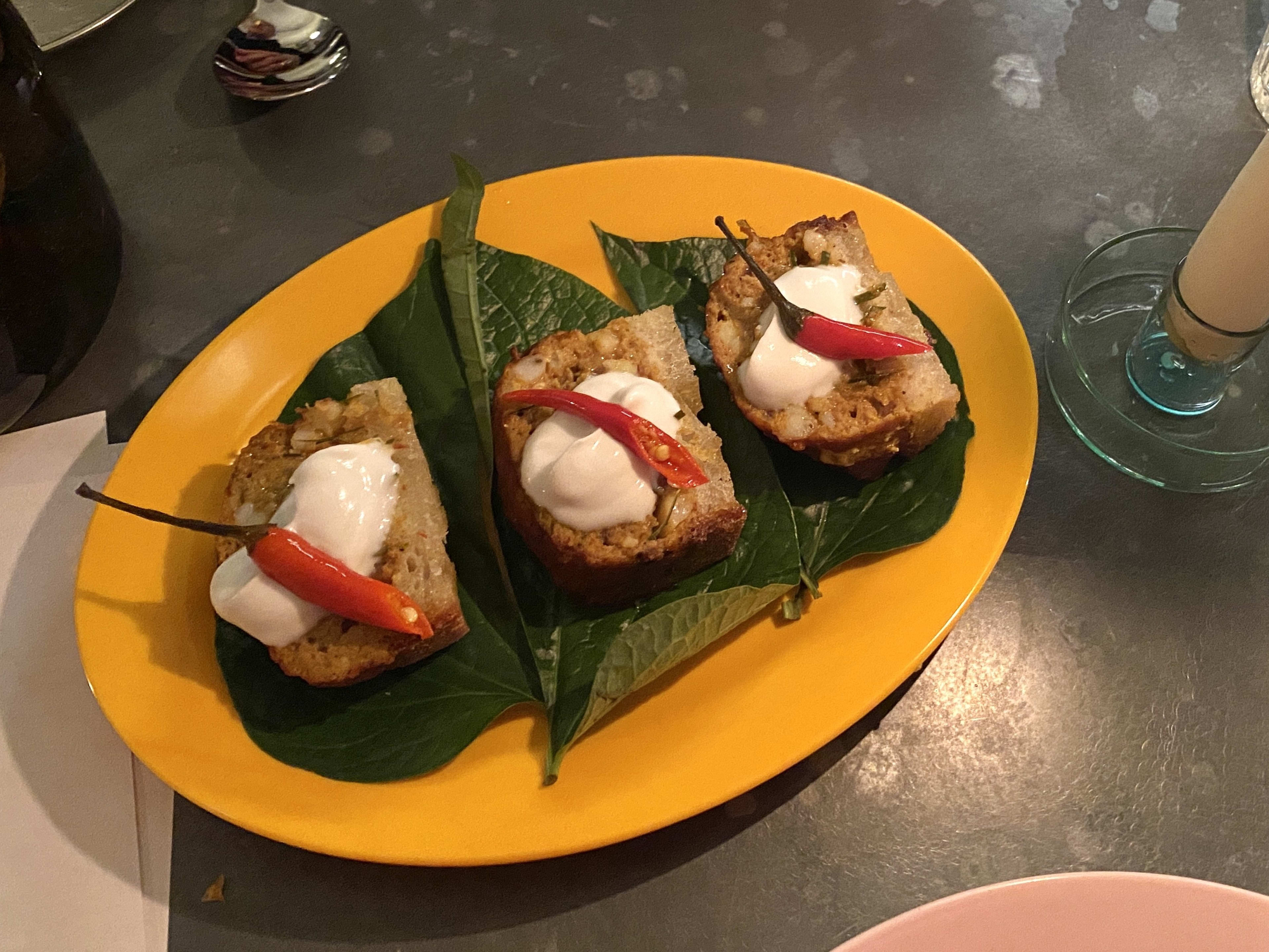 The prawn toast sitting on a betel leaf from Mambow on a bright yellow plastic plate.