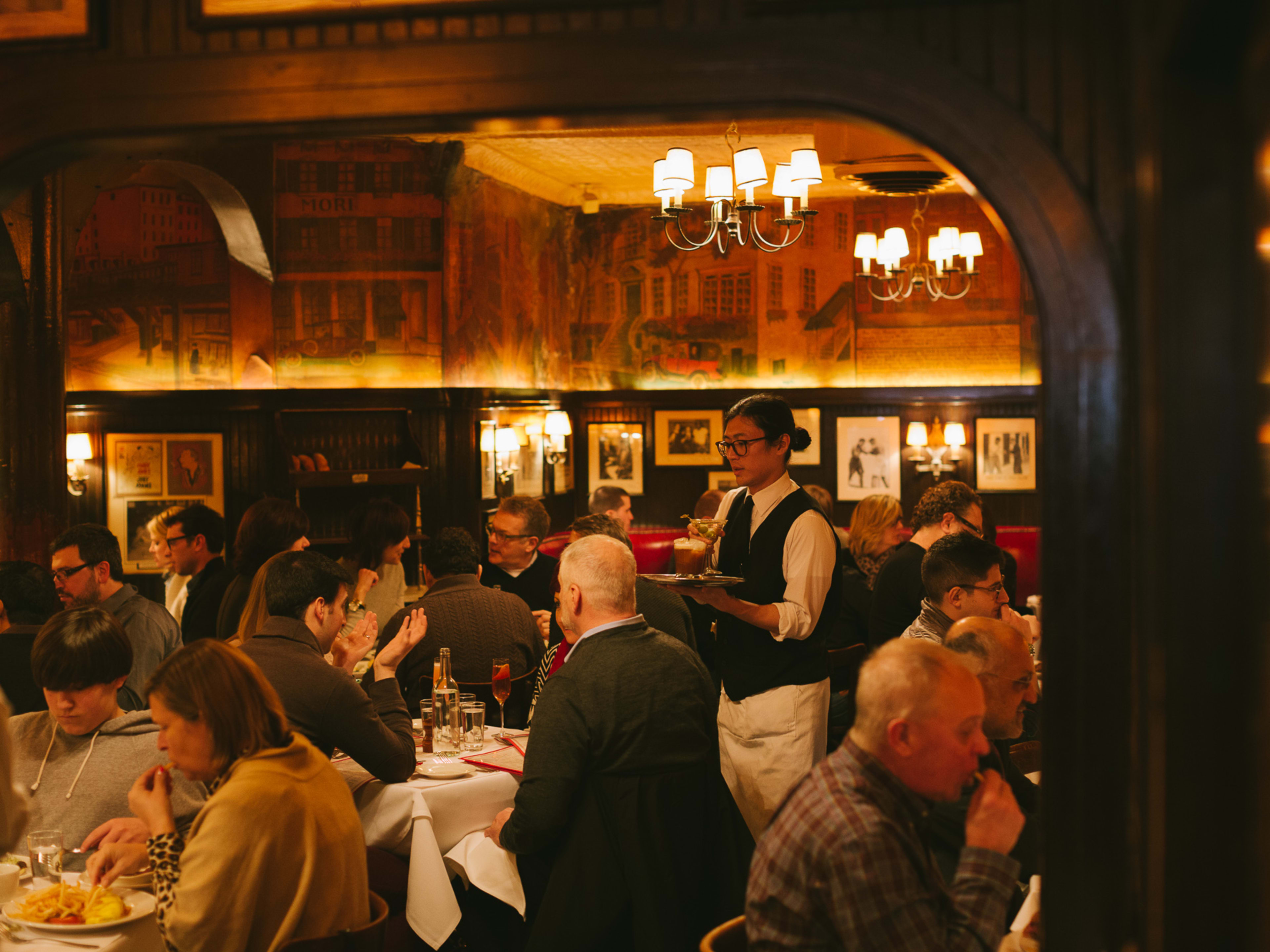 A dark, crowded dining room with yellowish lighting and servers in ties.