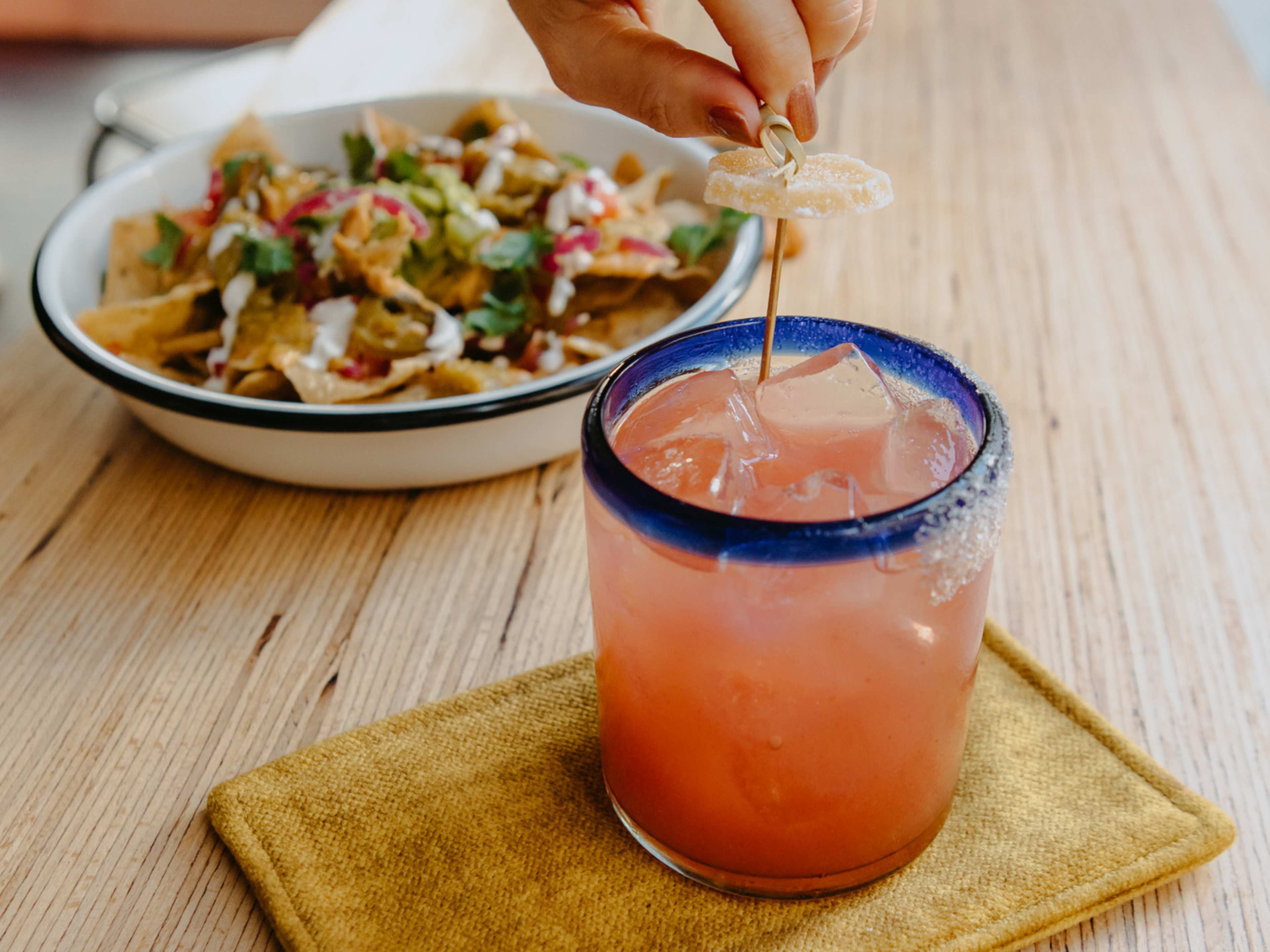 Cocktail with candied citrus garnish and plate of nachos at Abricot