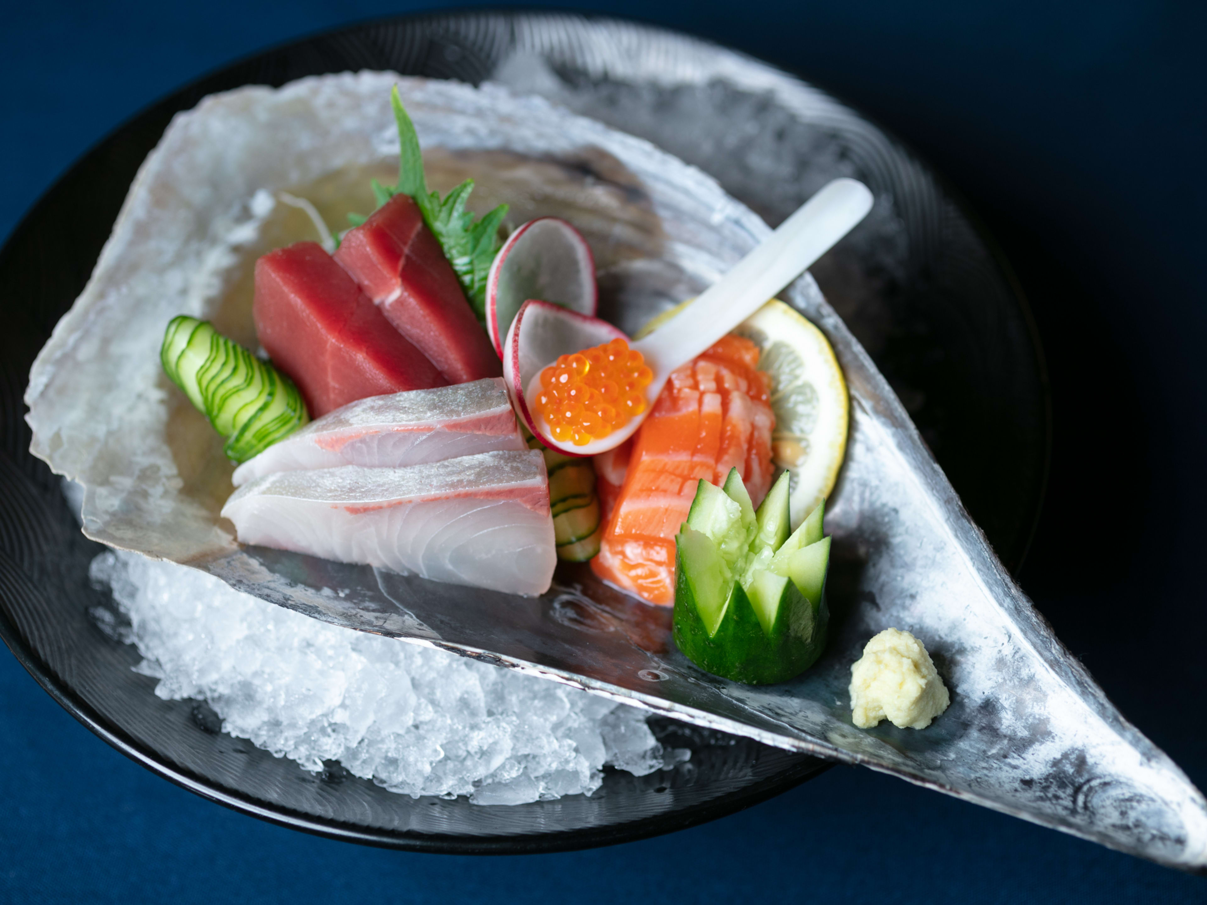 big shell on ice filled with sashimi and cucumber, and a spoon of roe