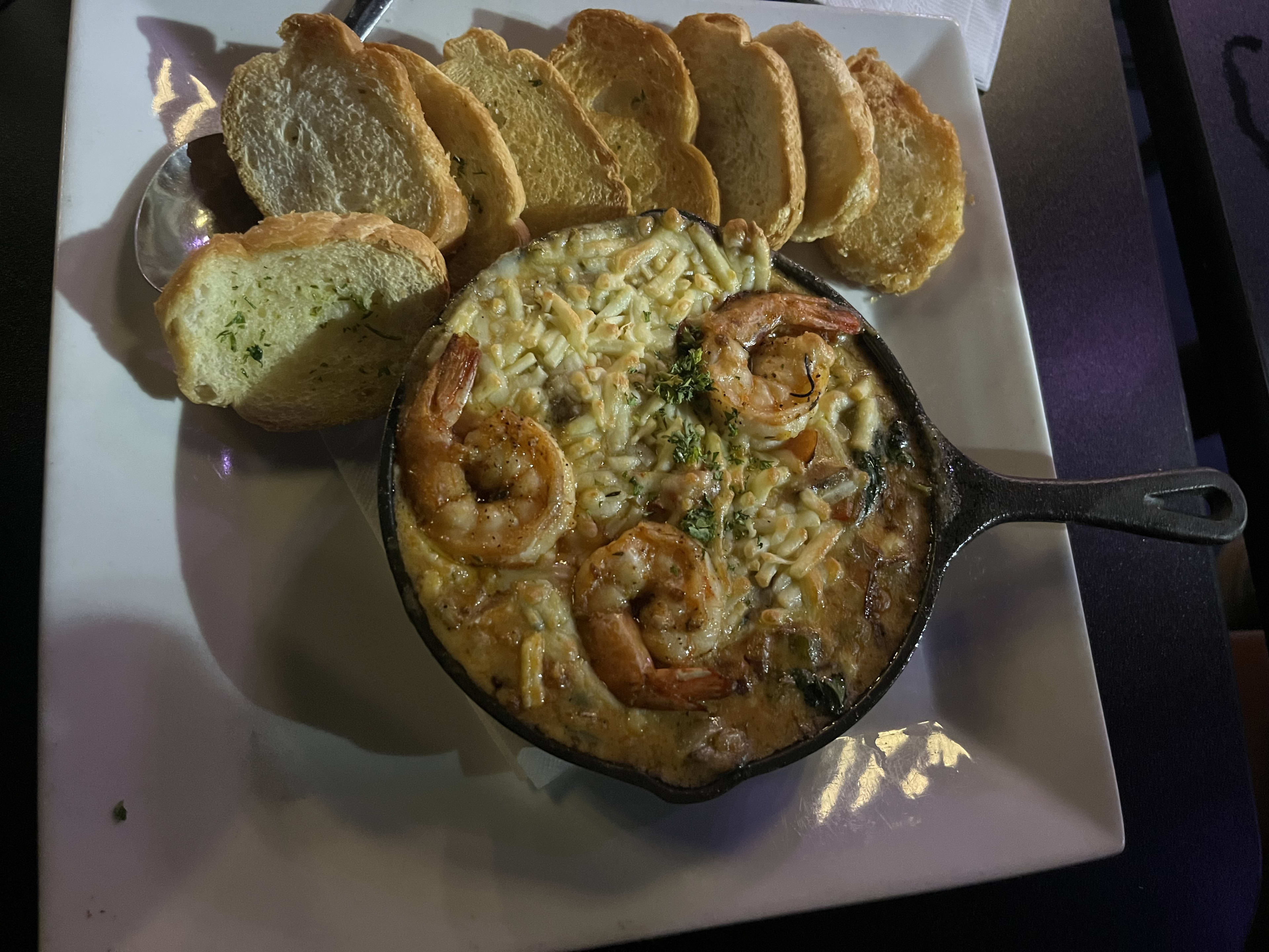 seafood fondue tipped with three pieces of shrimp and garlic bread on the side