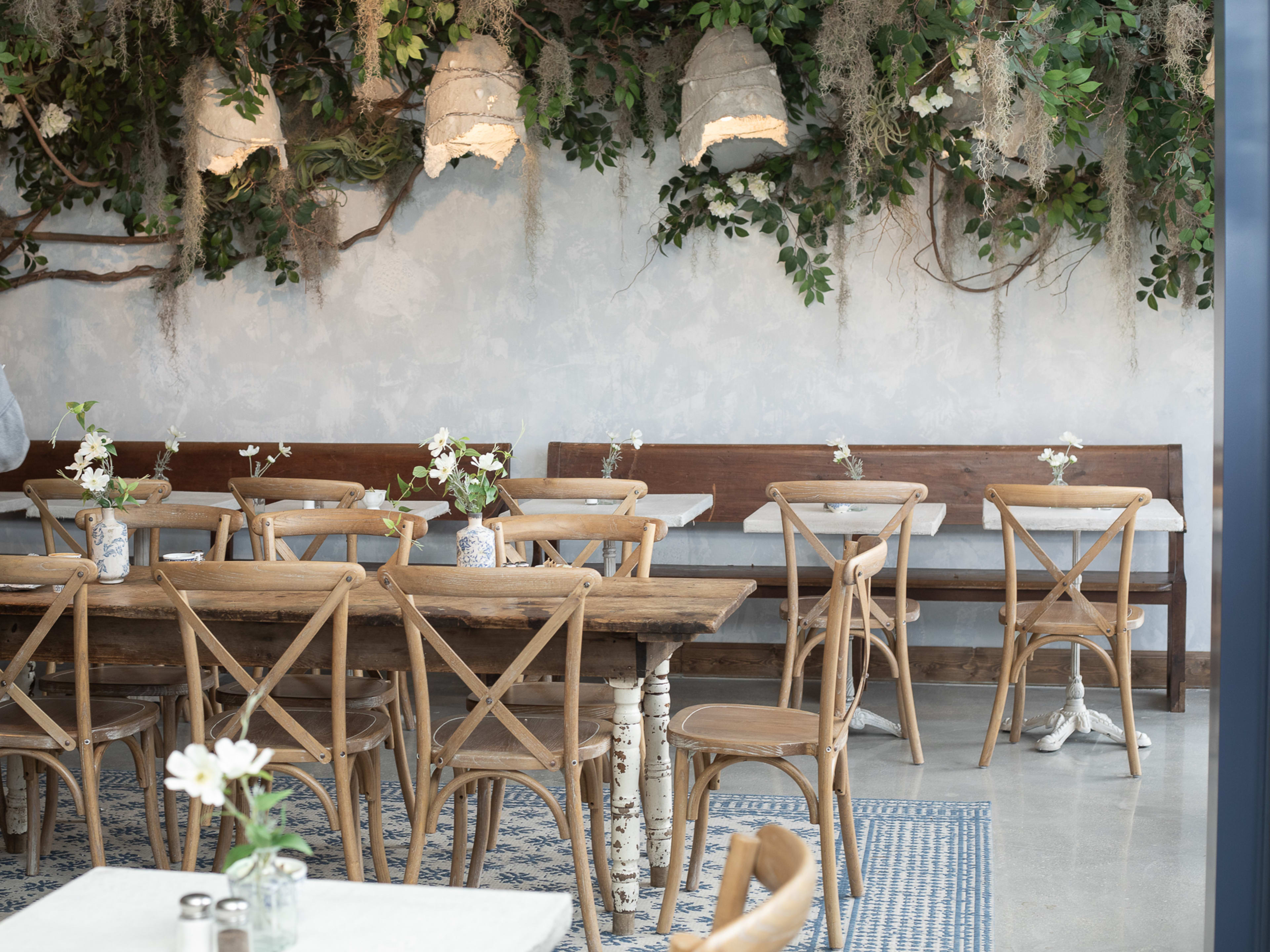 bright restaurant interior with light wood tables and greenery hanging from wall
