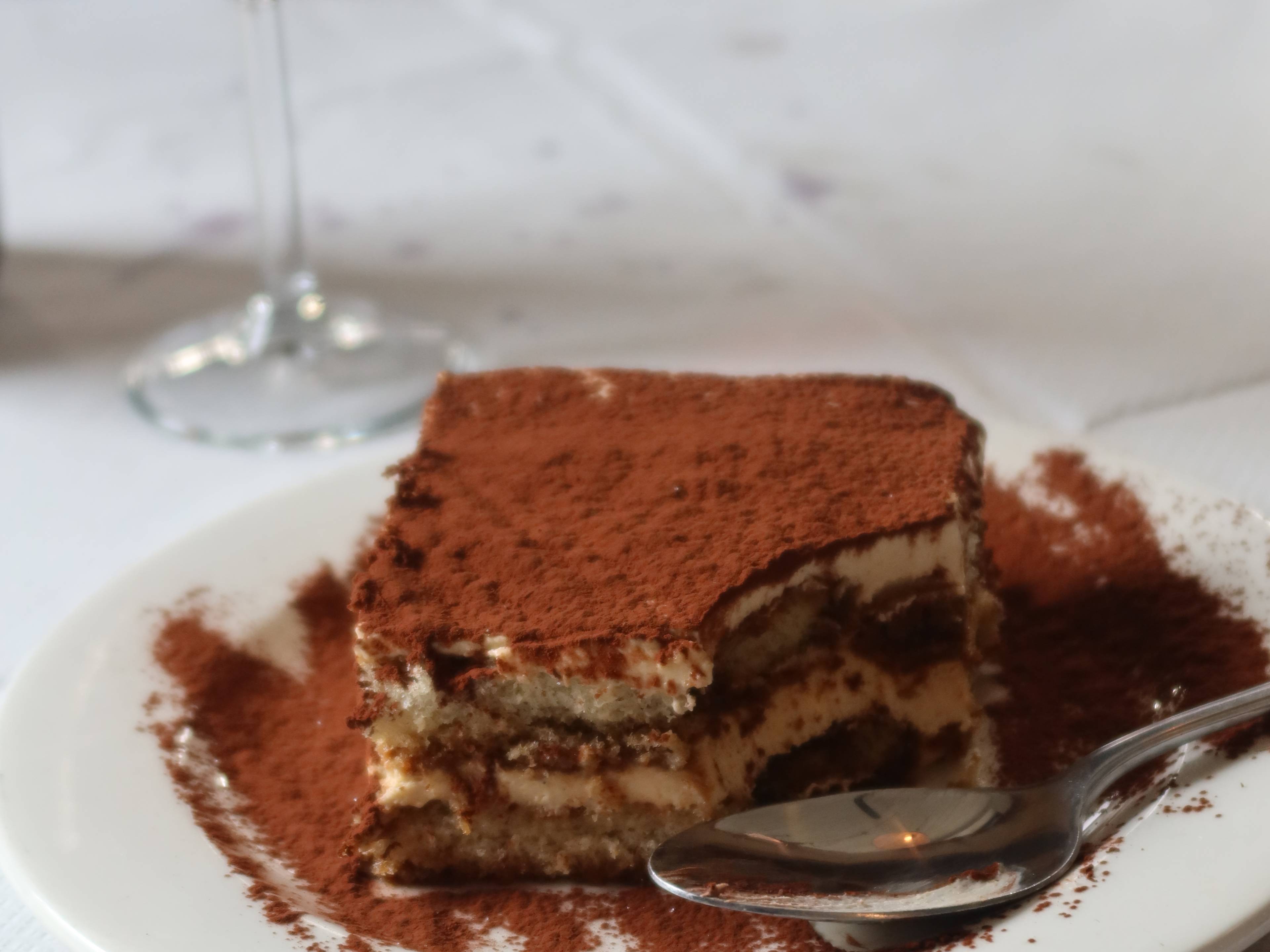 Tiramisu on a white plate, with a glass of red wine in the background.