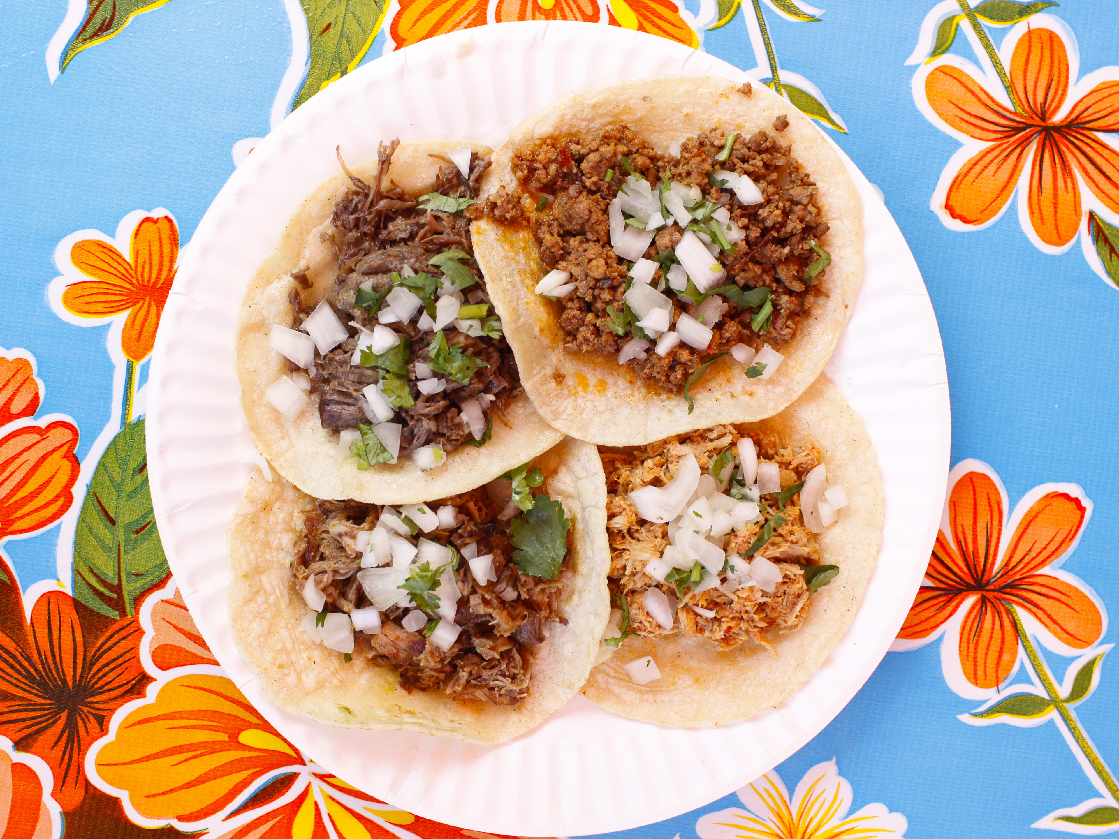 Paper plate with four tacos on a floral print table from La Fondita