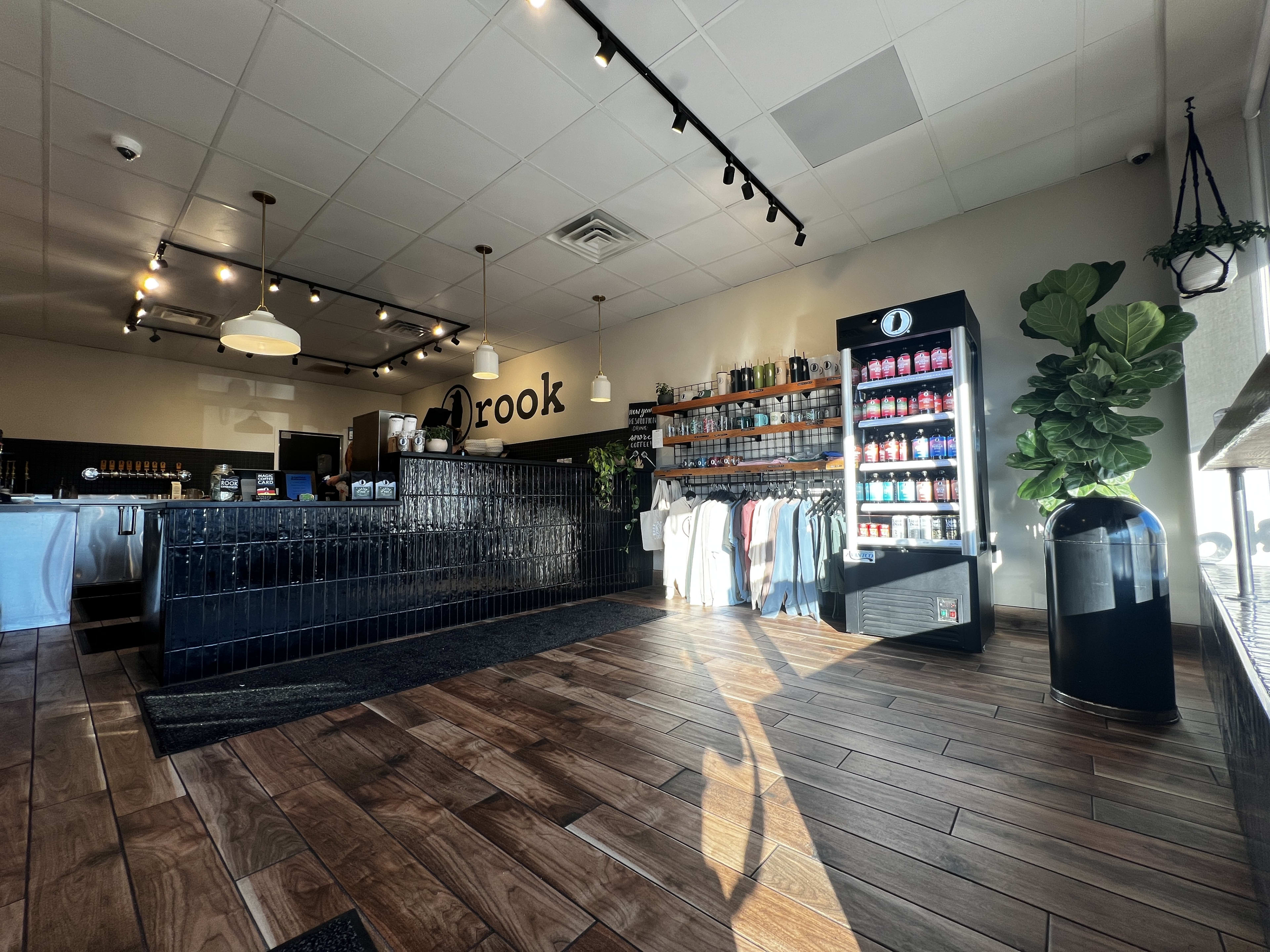 the inside of a coffee shop, with a wood-paneled floor, a fridge with drinks, and a counter where coffee is served