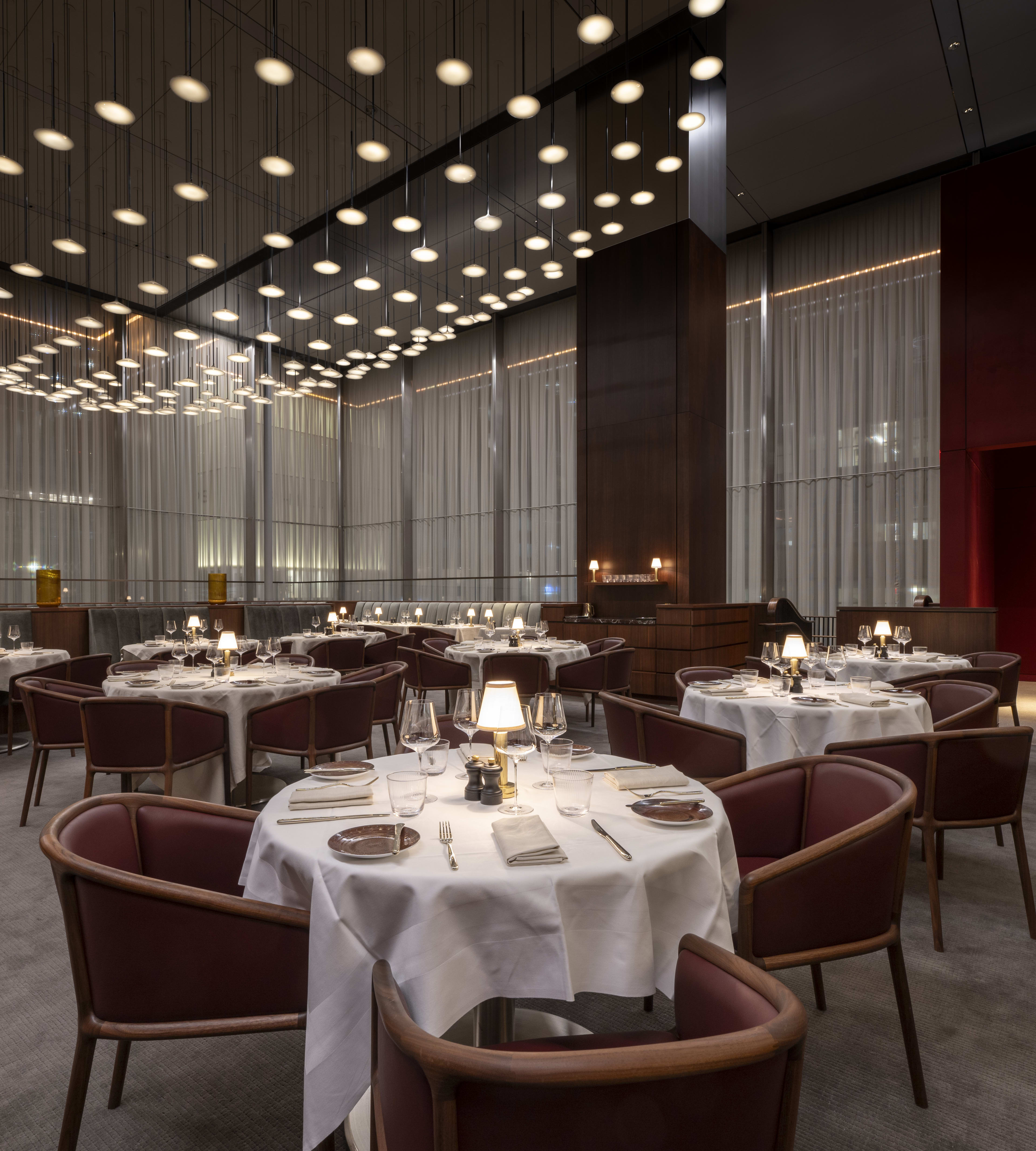 A carpeted dining room with white tablecloths and long sheer curtains on the windows.