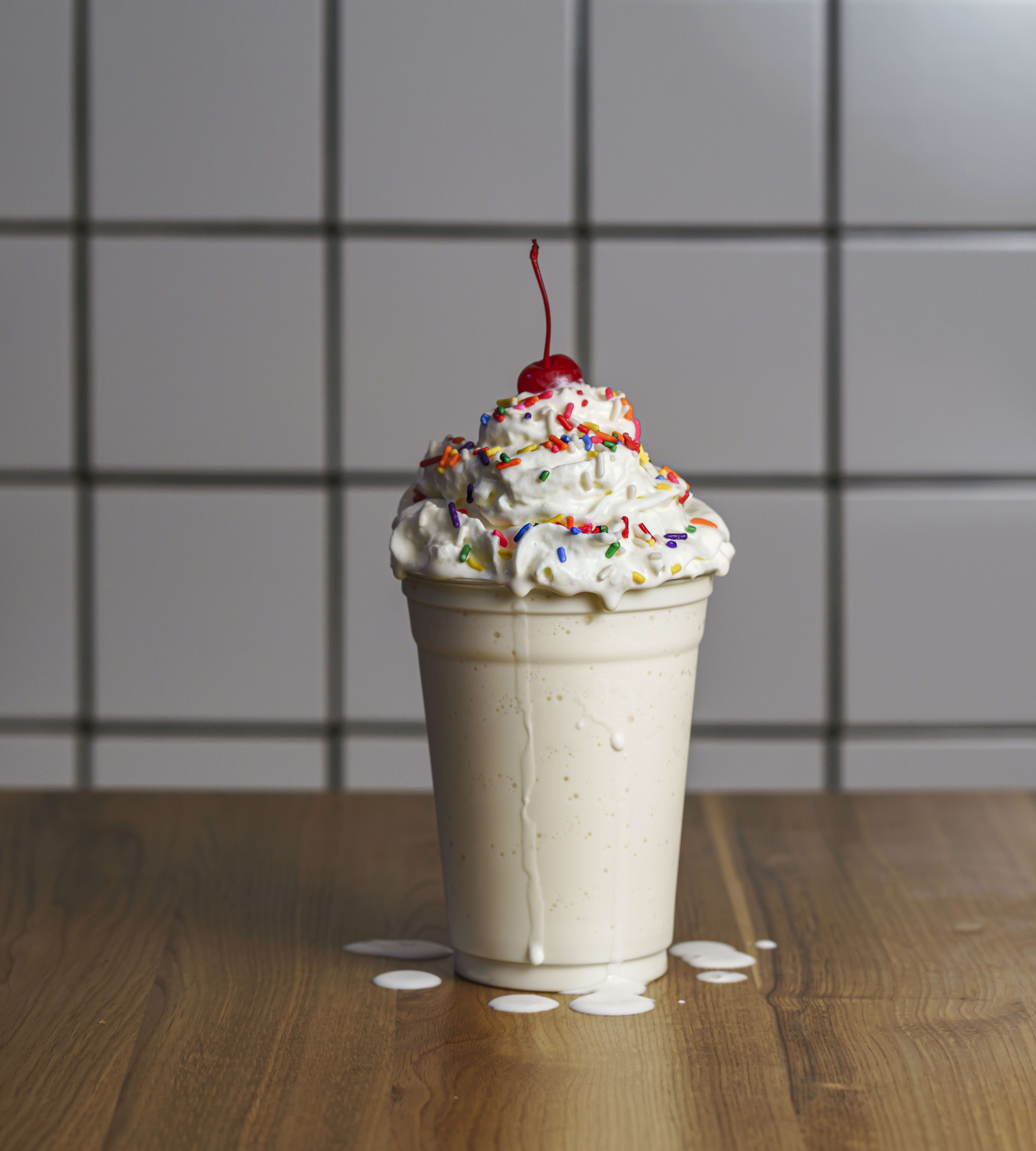 a vanilla milkshake with whipped cream, sprinkles, and a cherry