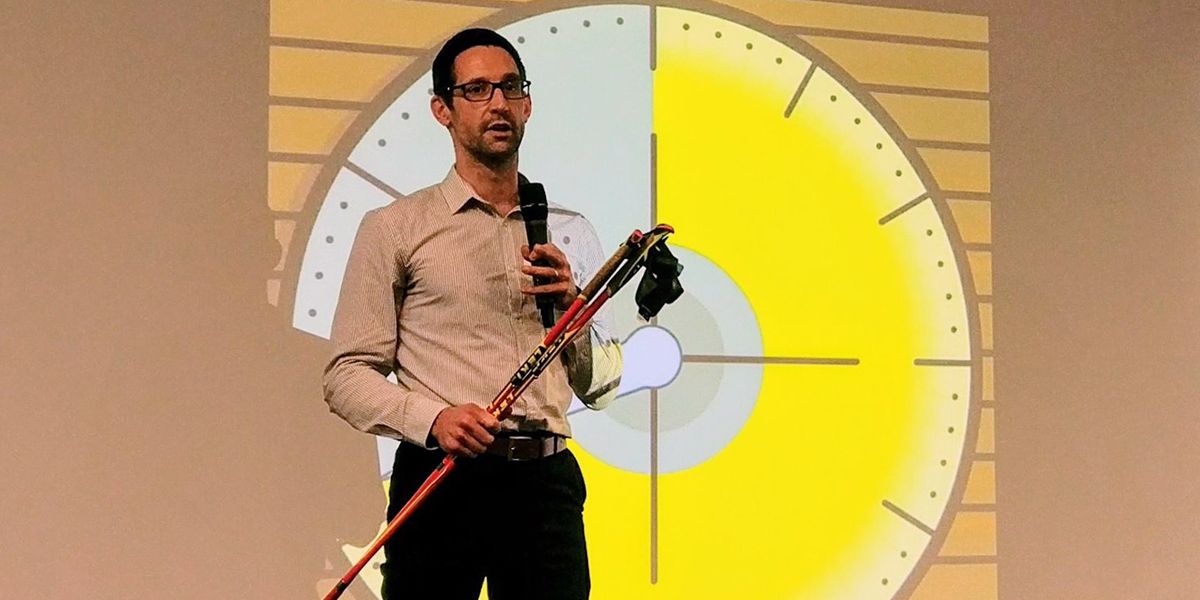 This is a picture of Matt Gibbs. Matt is a tall thin white man who wears glasses, a white shirt, black pants and is holding a set of Nordic Walking Poles