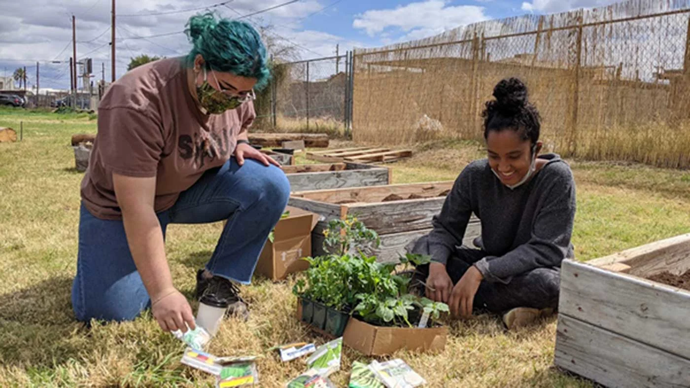 Two girls sitting in garden with plants and seeds in front of them.