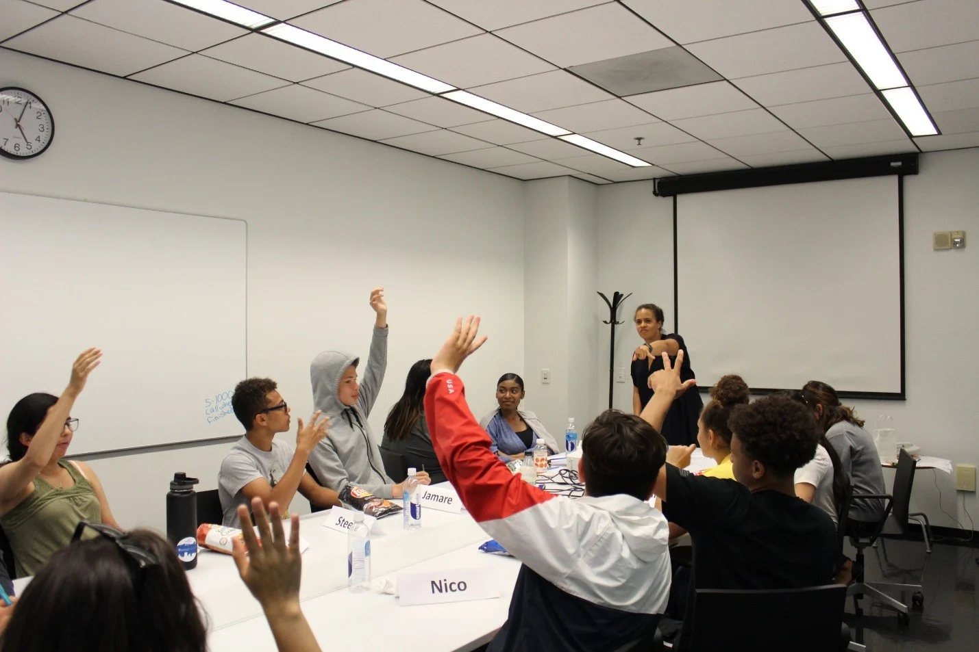 Amalia calls on a young person with their hand up at a table of students