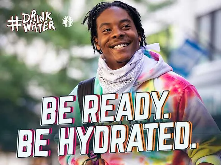 Man with colorful sweater on looking to the right and smiling with text Be read. Be hydrated. Hashtag drink water and the Seattle city logo.