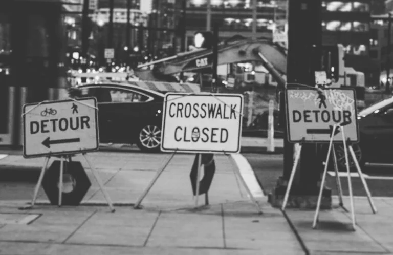 Street signs in an urban environment saying detour and crosswalk closed.