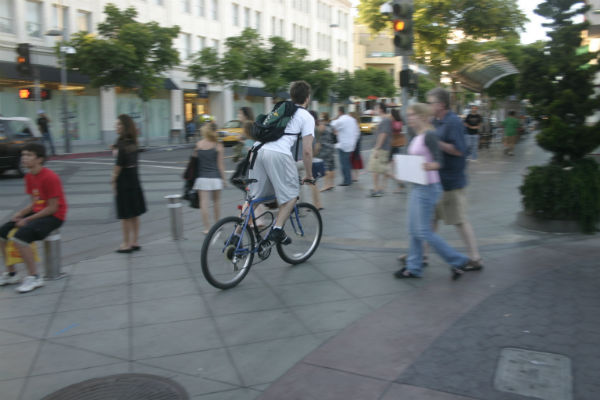 A cyclist, cycling through a street with pedestrians