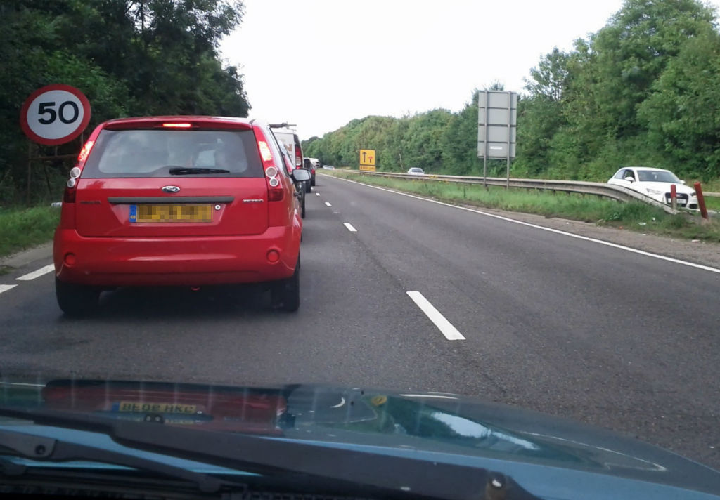 A queue of traffic with lane closed.  Drivers that push in at the front of the line