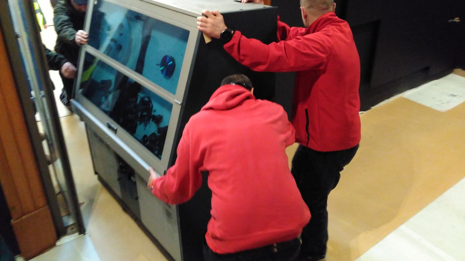 A group of people mainly dressed in red move a large piece of film equipment through a doorway