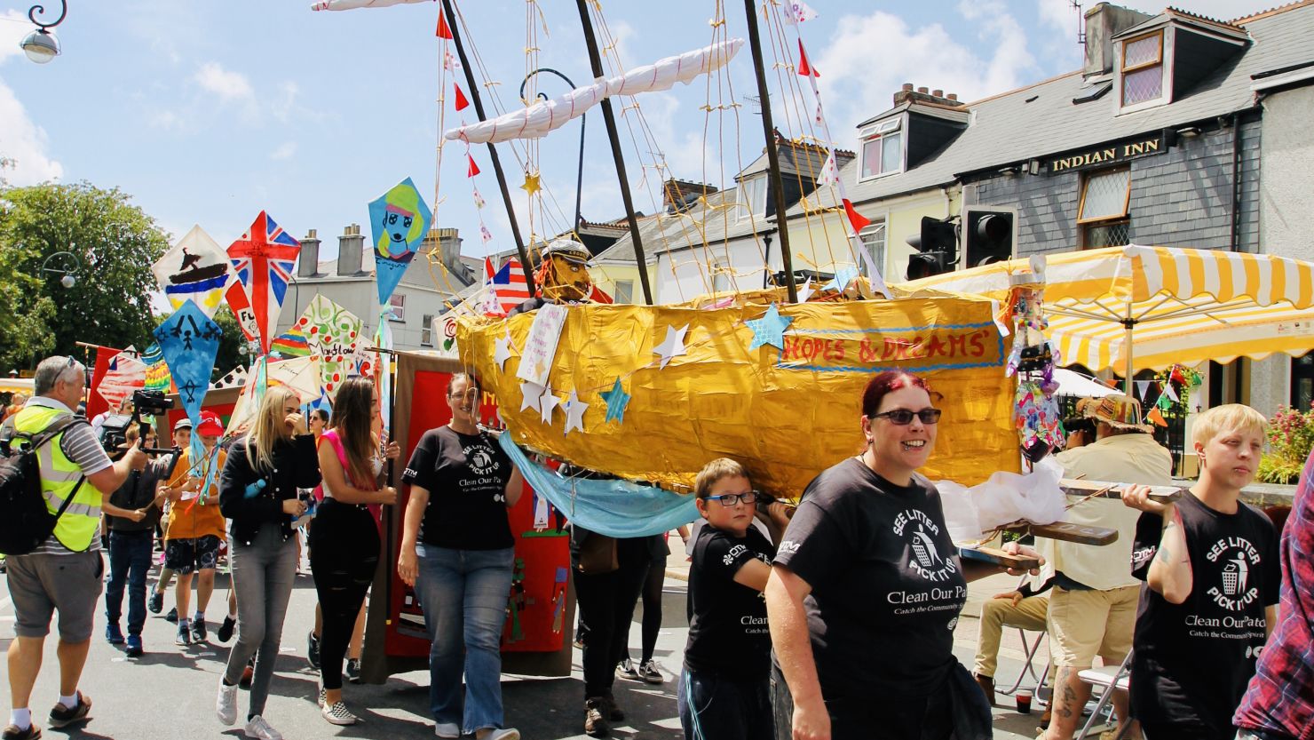 A group of people taking part in a community parade and carrying a boat made from card