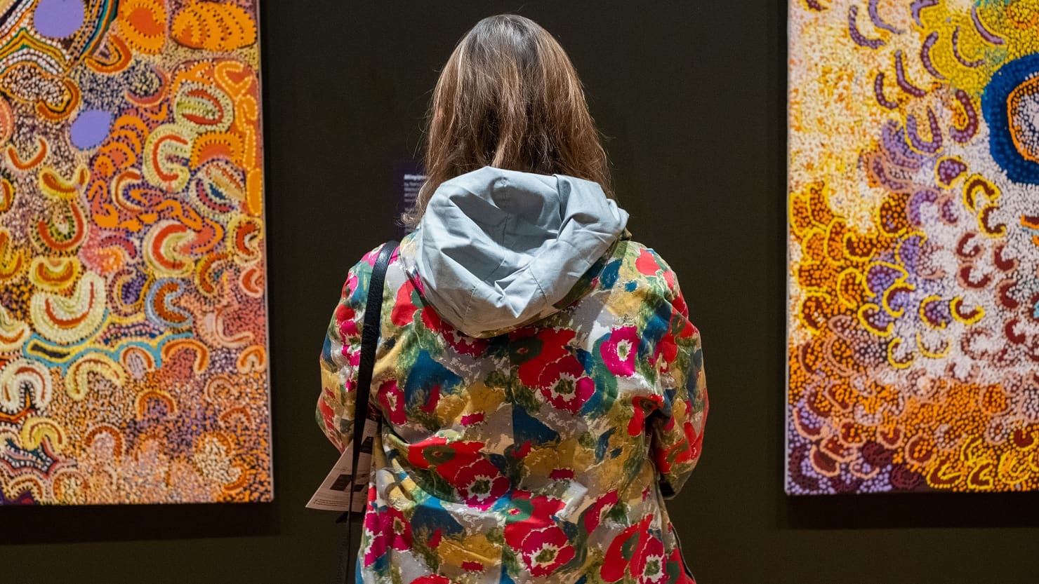 A woman stands between two paintings hanging on a wall. Image © Getty.