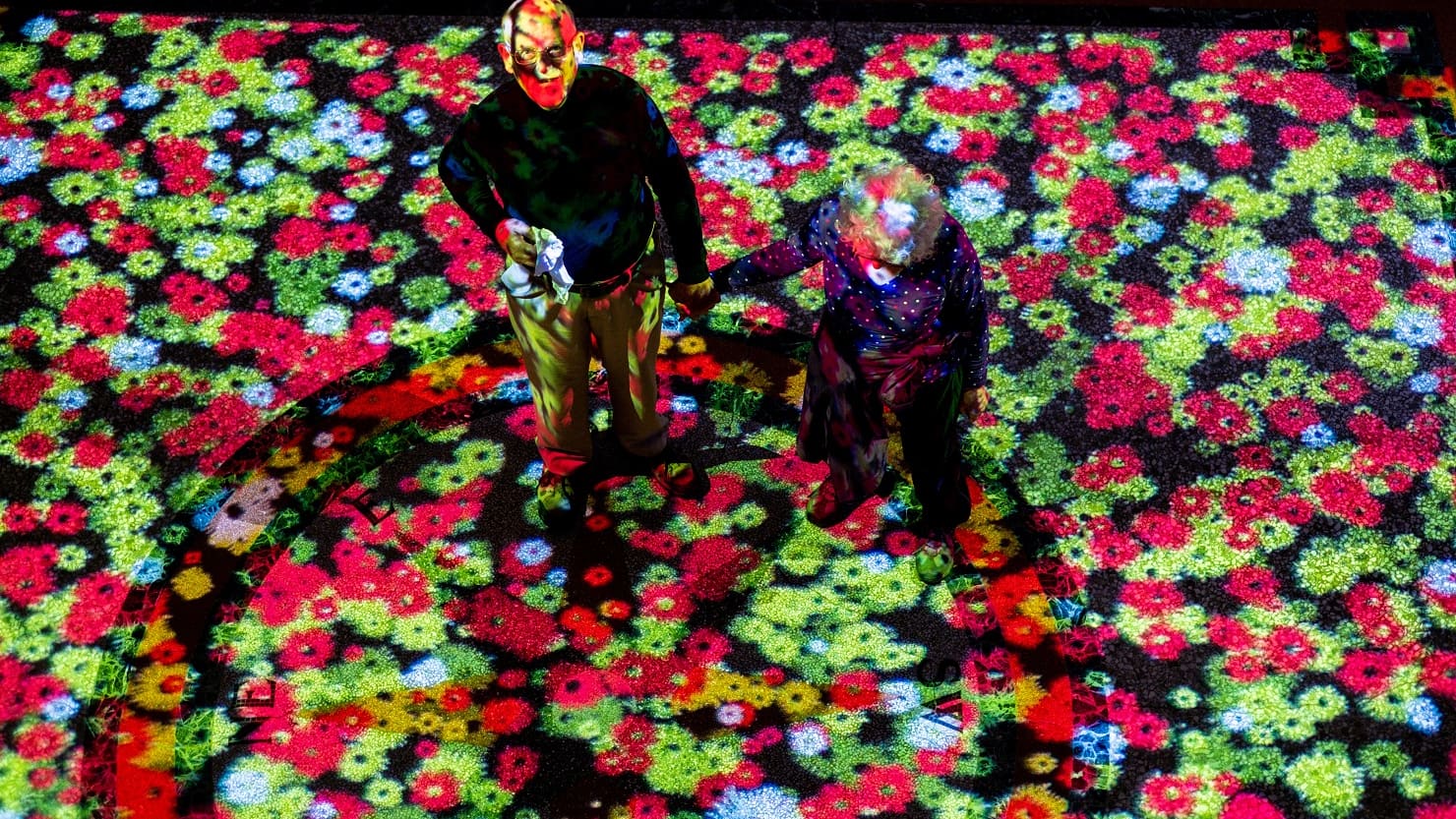 Two people walk through a digital projection of flowers. Image © Getty.