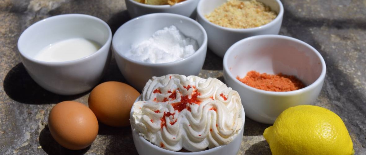 a lemon, eggs and small bowls of ingredients along with a baked Queen of Puddings