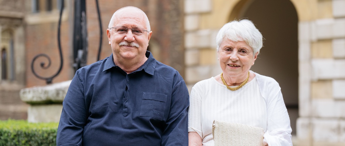 An older woman and man facing the camera with an historic building behind them
