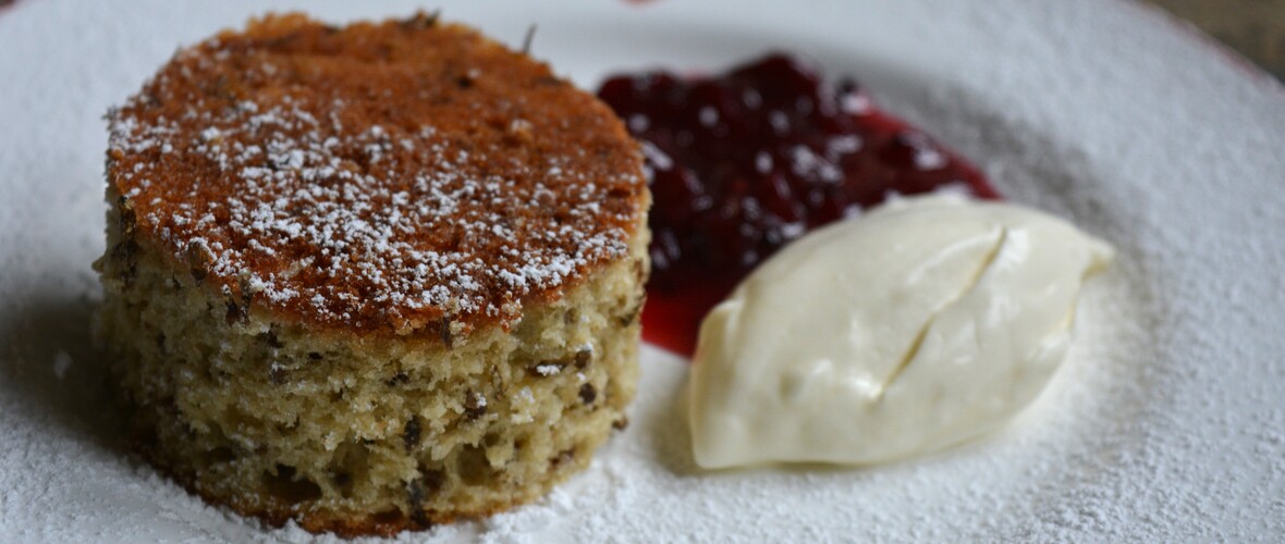 a cut our circle of lavender sponge on a white plate with a berry compote and a quenelle of cream