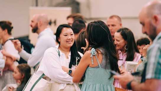 A smiling woman greets people in a crowded lobby before a Sunday service at New Heights Community Church.