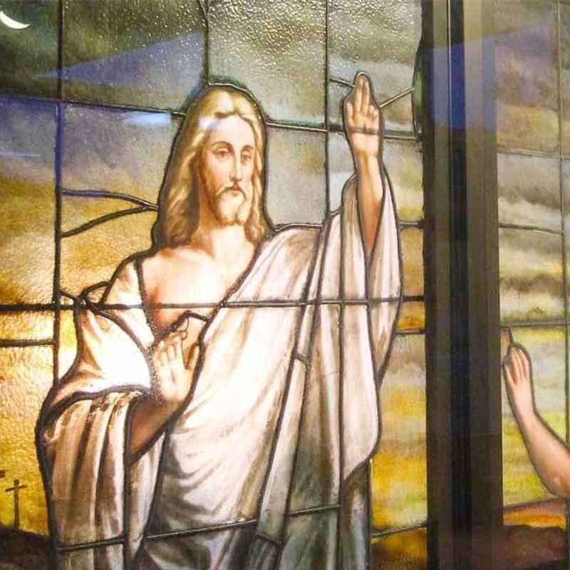 A colorful stained glass window showing Jesus with his hand raised in blessing. A follower looks up at him, and three crosses are visible in the background.