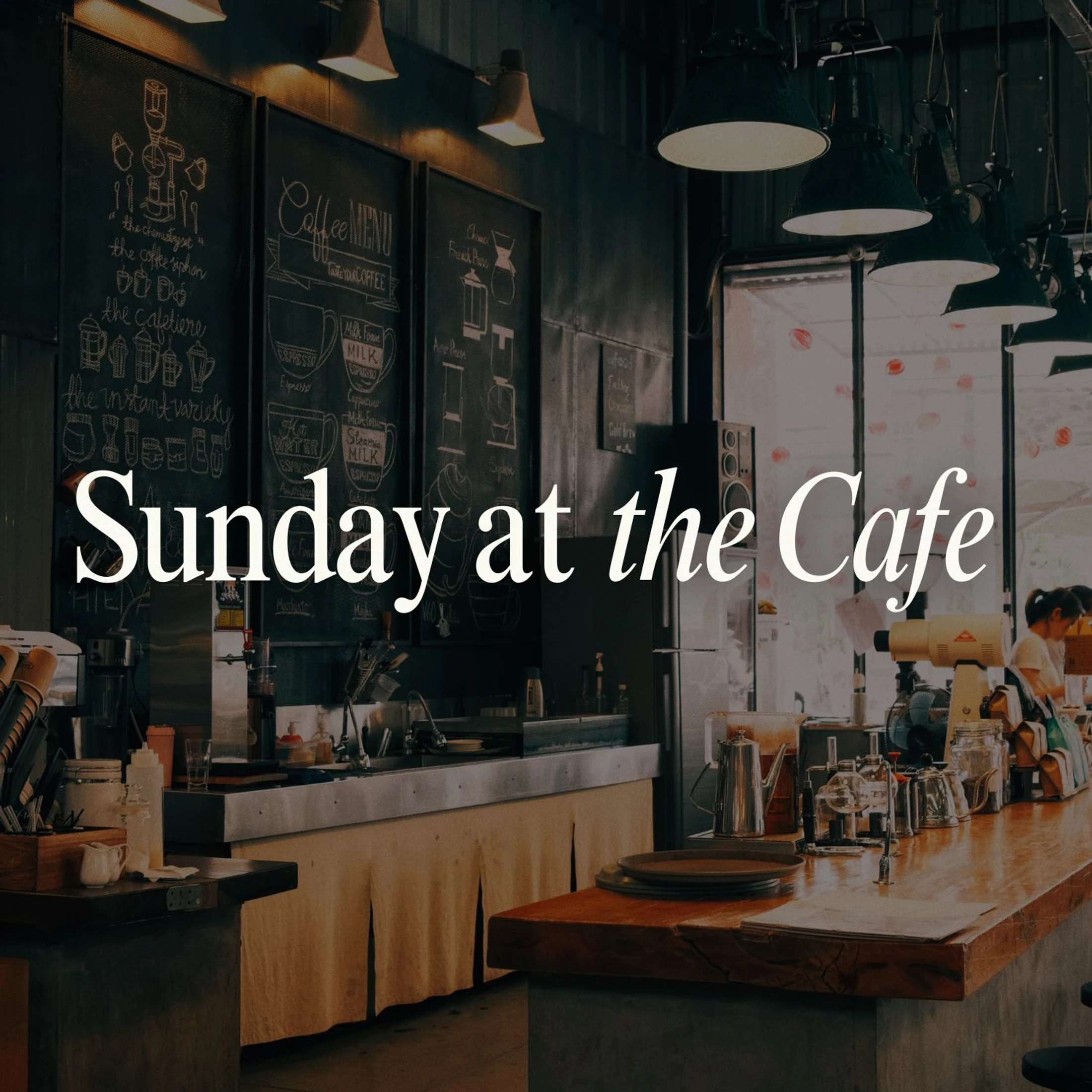 The dimly lit interior of a rustic coffee shop. A wooden counter is in the foreground, with a large chalkboard menu on the wall behind it.