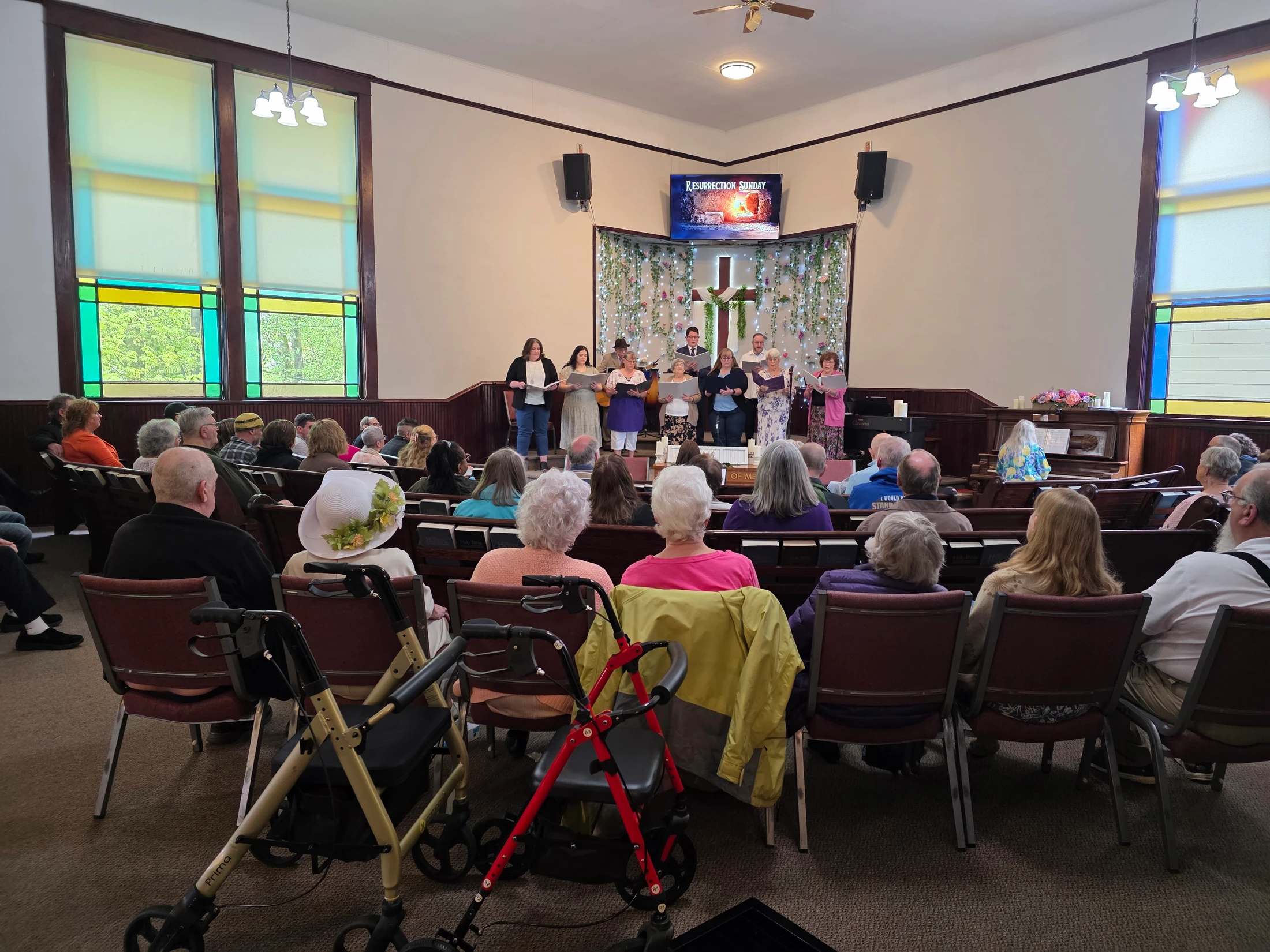 View from the back of a church showing the congregation watching a choir sing on a decorated stage during a Resurrection Sunday service.