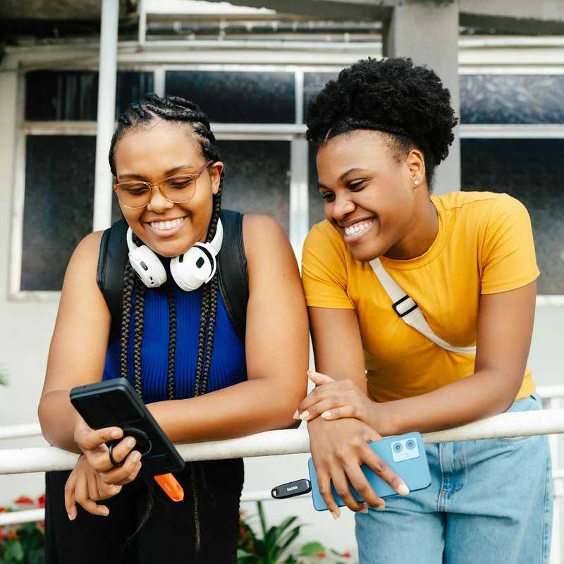 Two smiling women looking at a smartphone outdoors