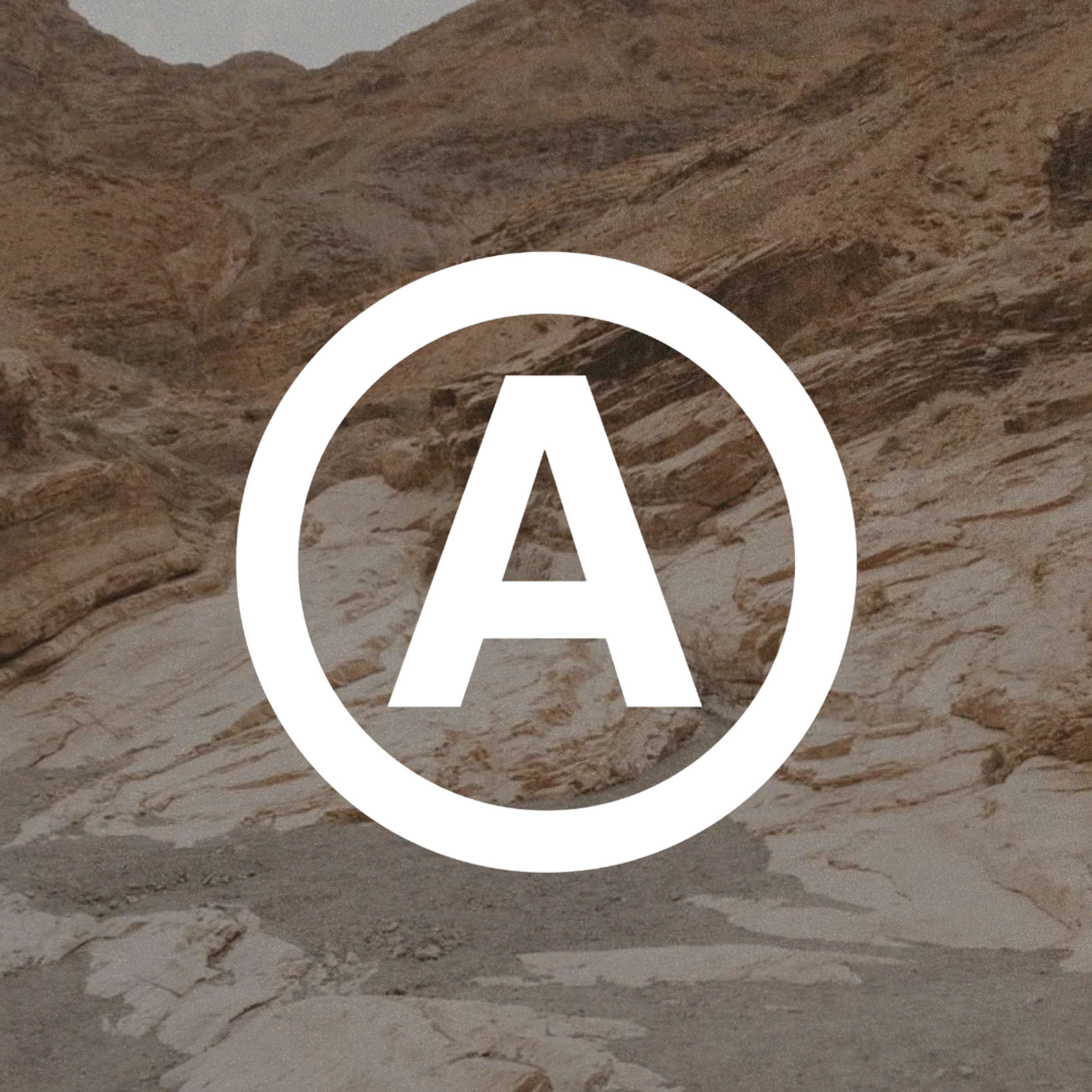 The white anarchist symbol, a capital letter A inside a circle, is superimposed over a photo of a rocky, brown, mountainous landscape.