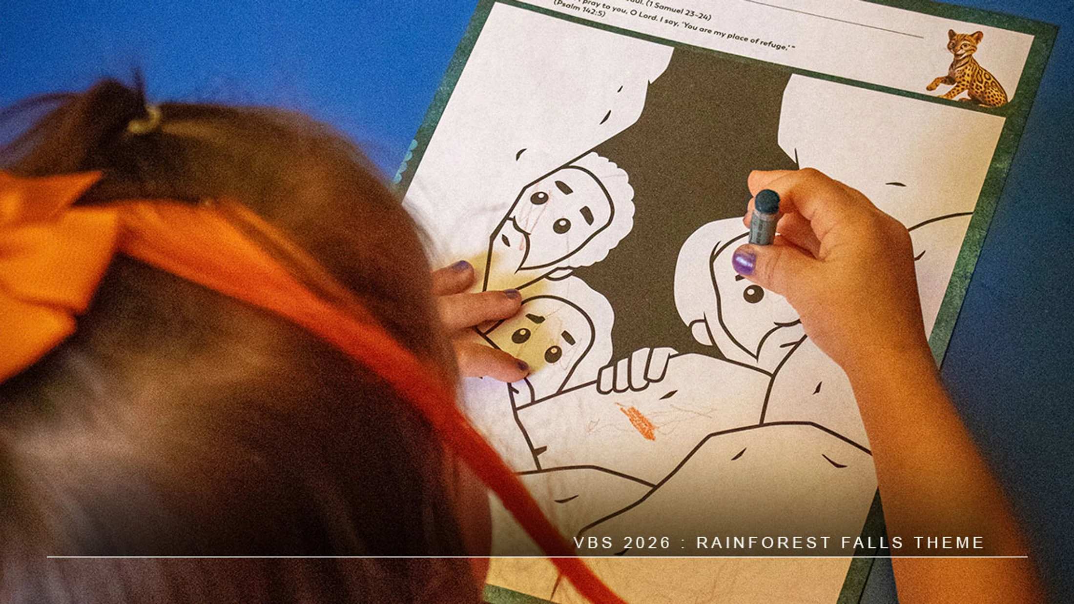 An over-the-shoulder view of a young girl with an orange bow in her hair, using a blue crayon to color a worksheet during a VBS activity.