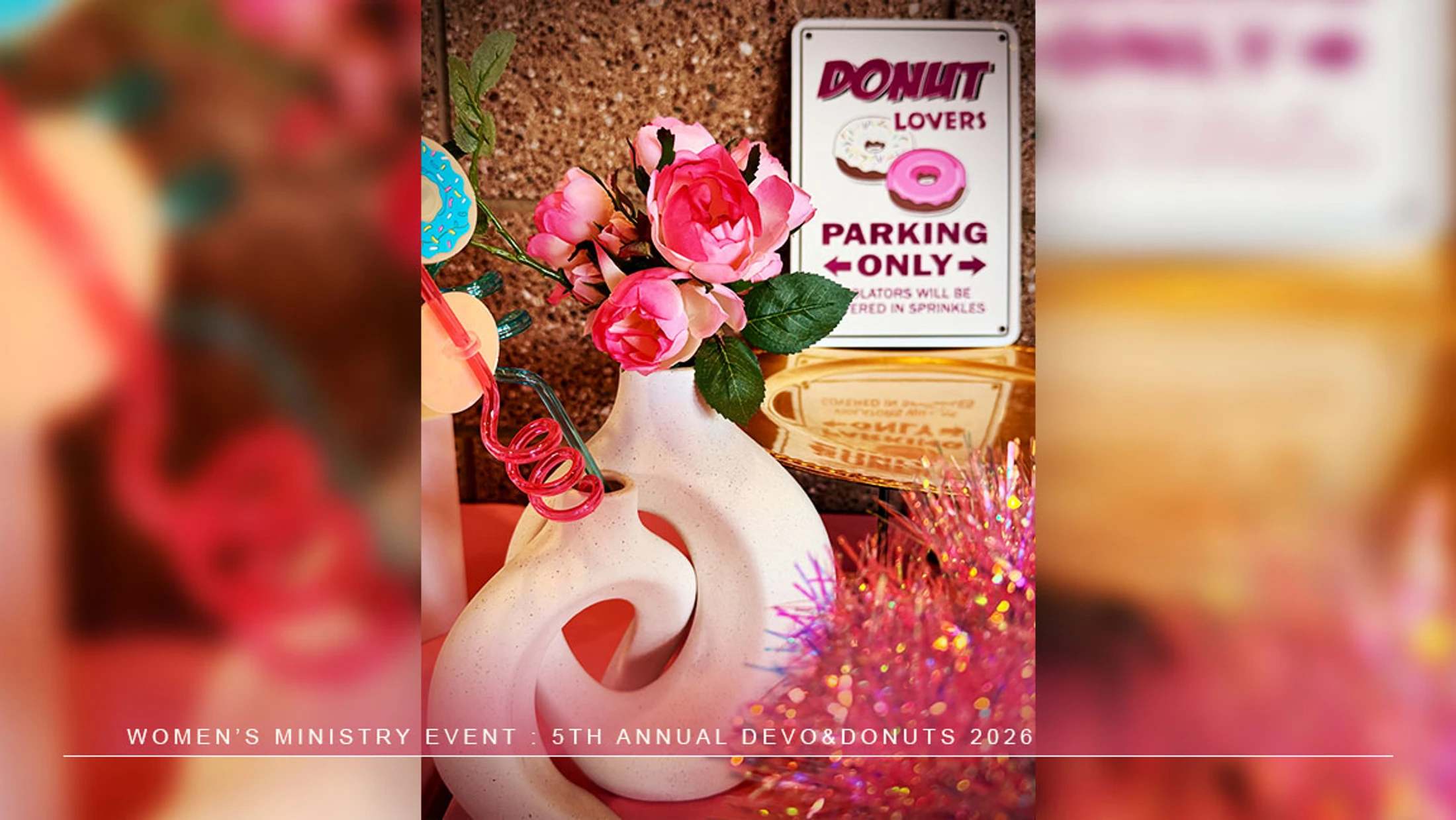 Decorations for a 'Devo & Donuts' event, featuring a white vase with pink flowers and a 'Donut Lovers Parking Only' sign.