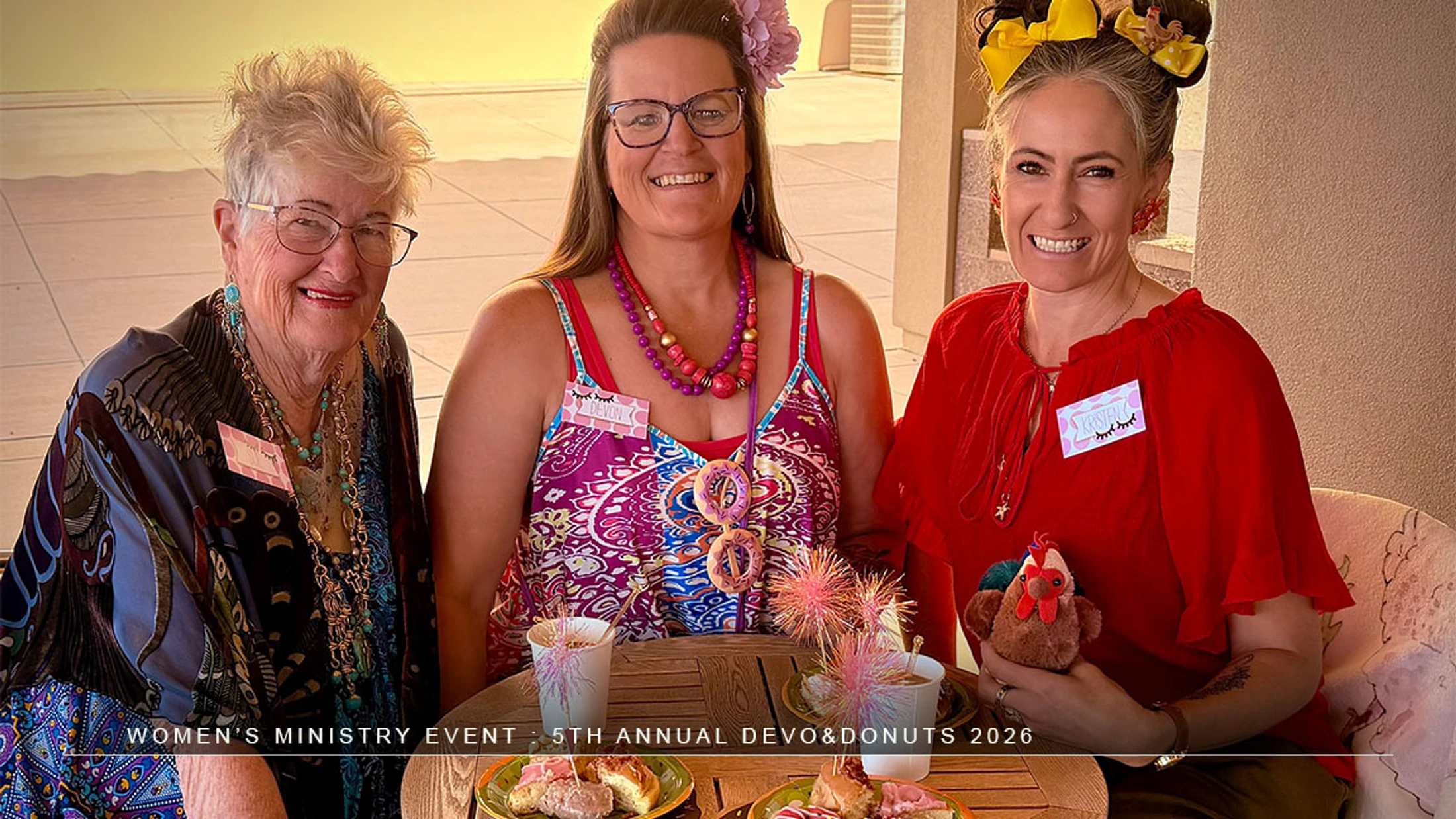 Three women smile for a photo while seated at a table with coffee and donuts during the 5th Annual Devo & Donuts Women's Ministry event.
