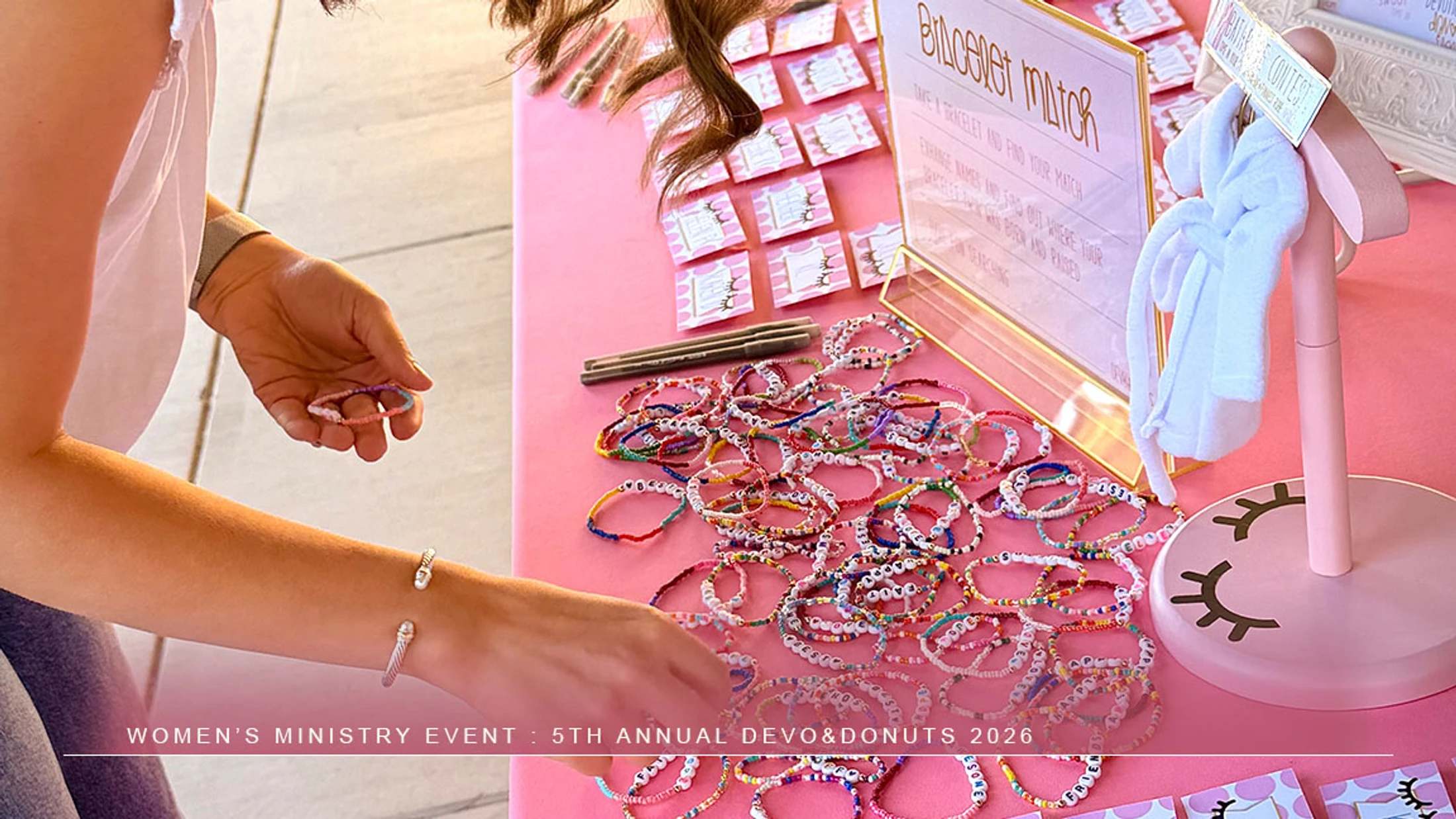 A woman reaches for colorful beaded bracelets on a pink table during an icebreaker game at the 5th Annual Devo & Donuts women's ministry event.