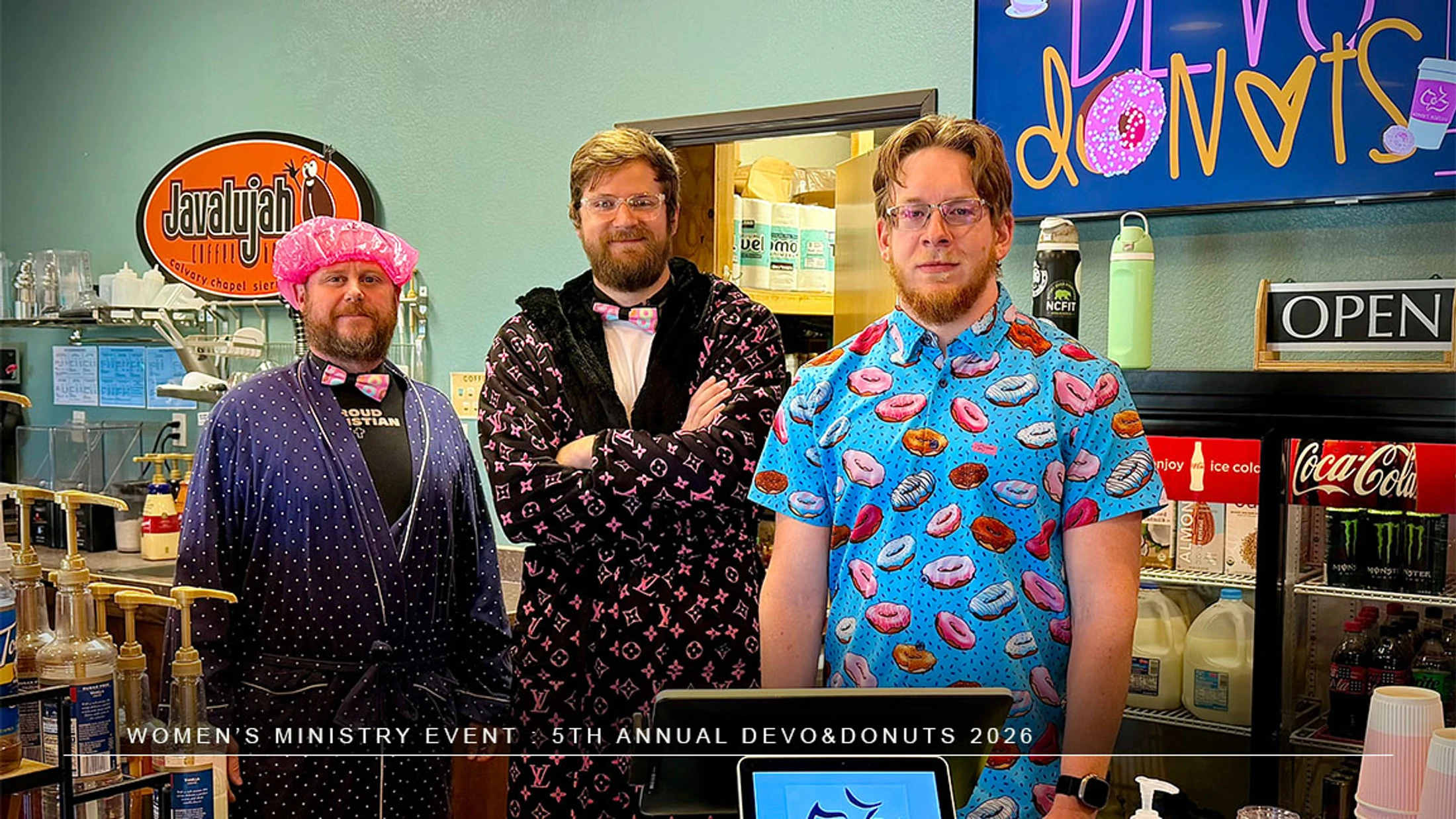Three men in humorous, themed outfits, including robes and a donut shirt, stand behind a counter at a coffee shop for a 'Devo & Donuts' women's ministry event.