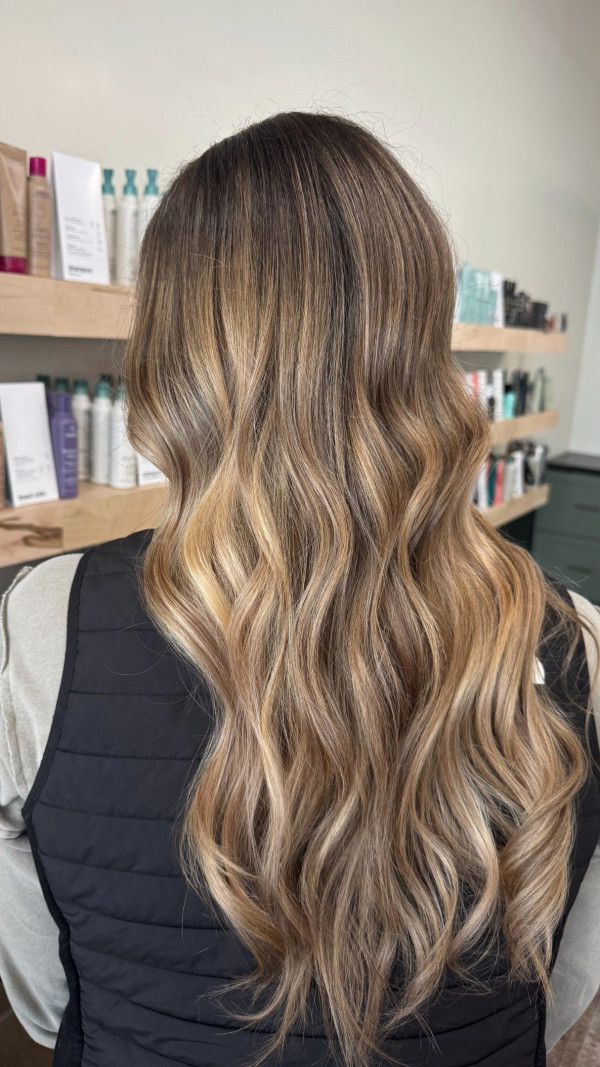 Long wavy brunette hair with soft blonde balayage highlights and dimensional salon color blend.