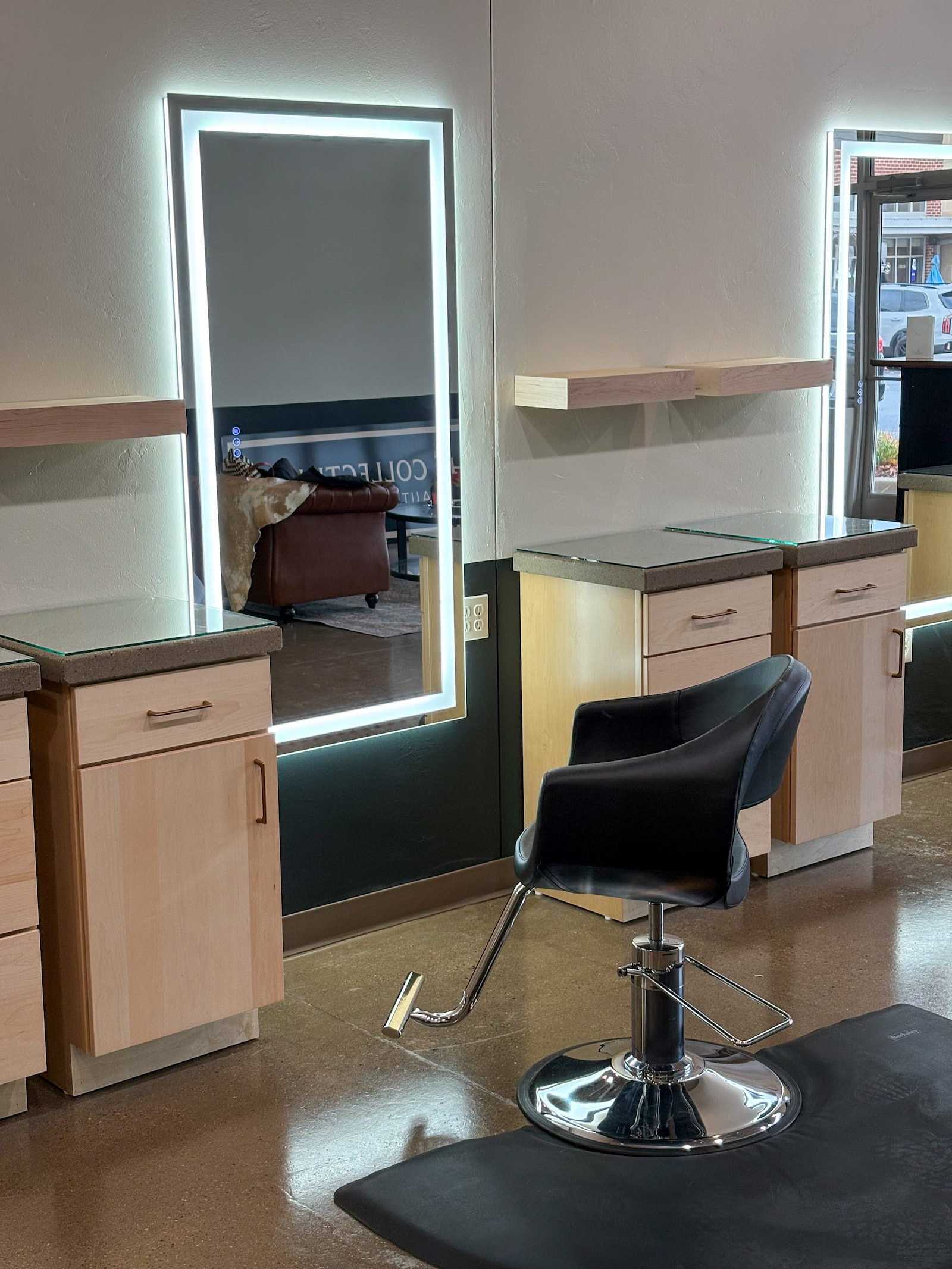 Close-up of salon styling station in Green Bay WI with LED mirror, black chair, and maple cabinetry.