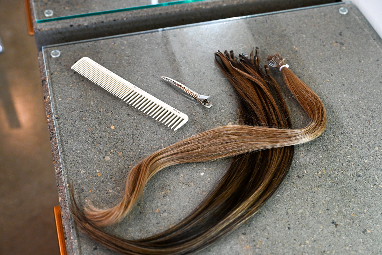 Hair extension wefts arranged with a comb and sectioning clip, prepared for a professional extension service at The Collective in Green Bay, Wisconsin.