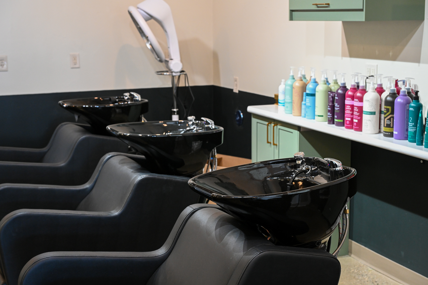 Modern shampoo area with black wash bowls and professional hair care products inside The Collective luxury salon in Green Bay, Wisconsin.