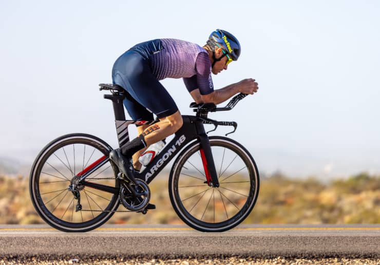 Triathlete in an aero position on a bike, wearing a The Feed aero helmet