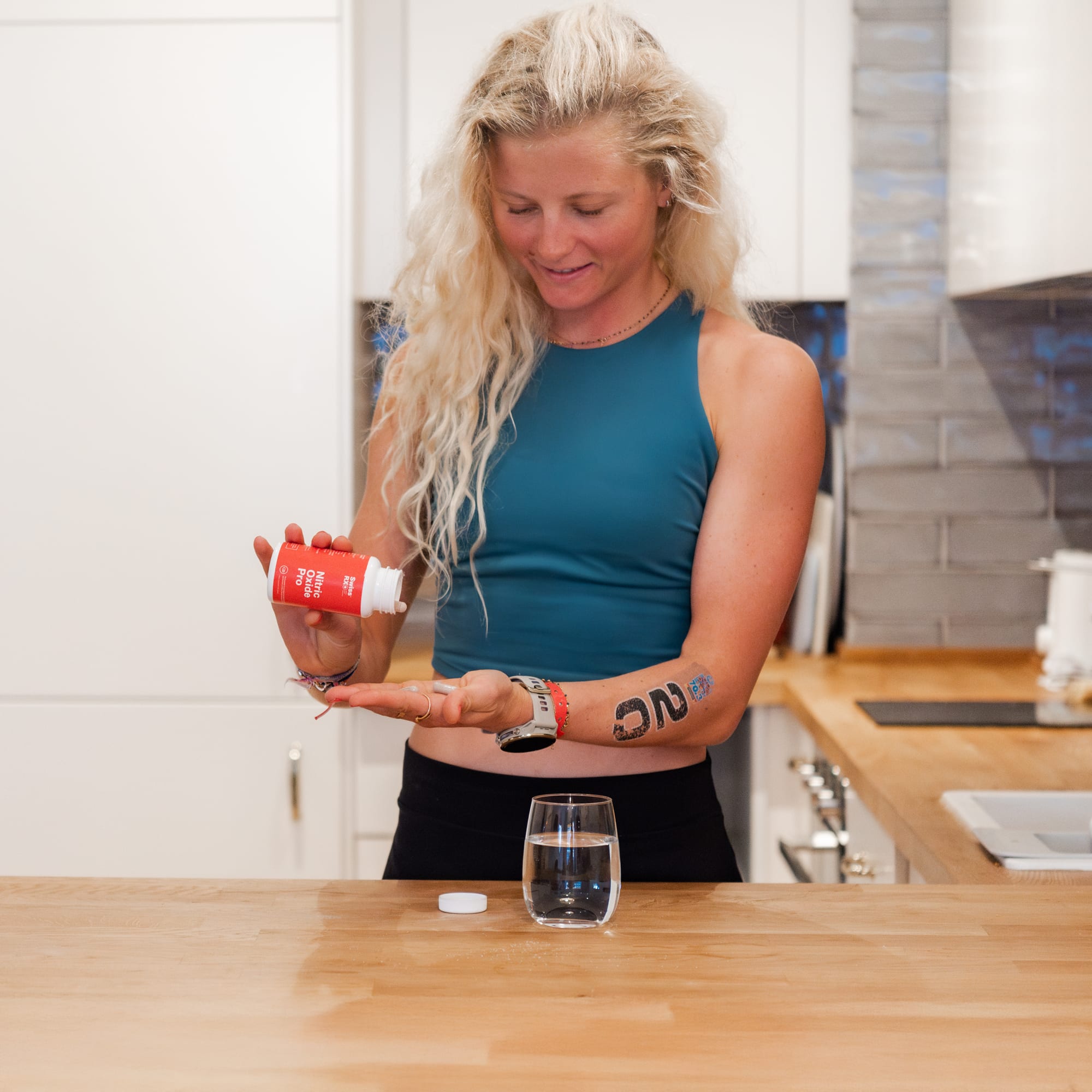 Female endurance athlete taking SwissRX Nitric Oxide Pro supplement tablets before training in kitchen