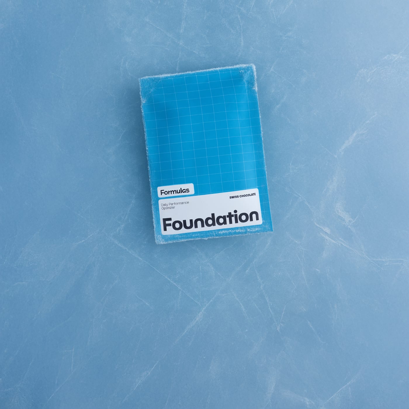 Foundation daily performance optimizer single-serve packet resting on a frozen ice surface, lightly frosted edges with a clean blue winter background
