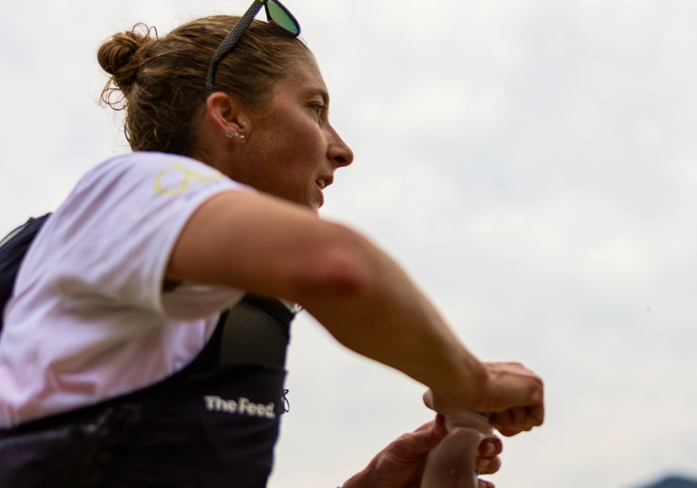 Courtney Dauwalter in profile wearing sunglasses and a white running shirt with "The Feed" logo, focused and determined during a race