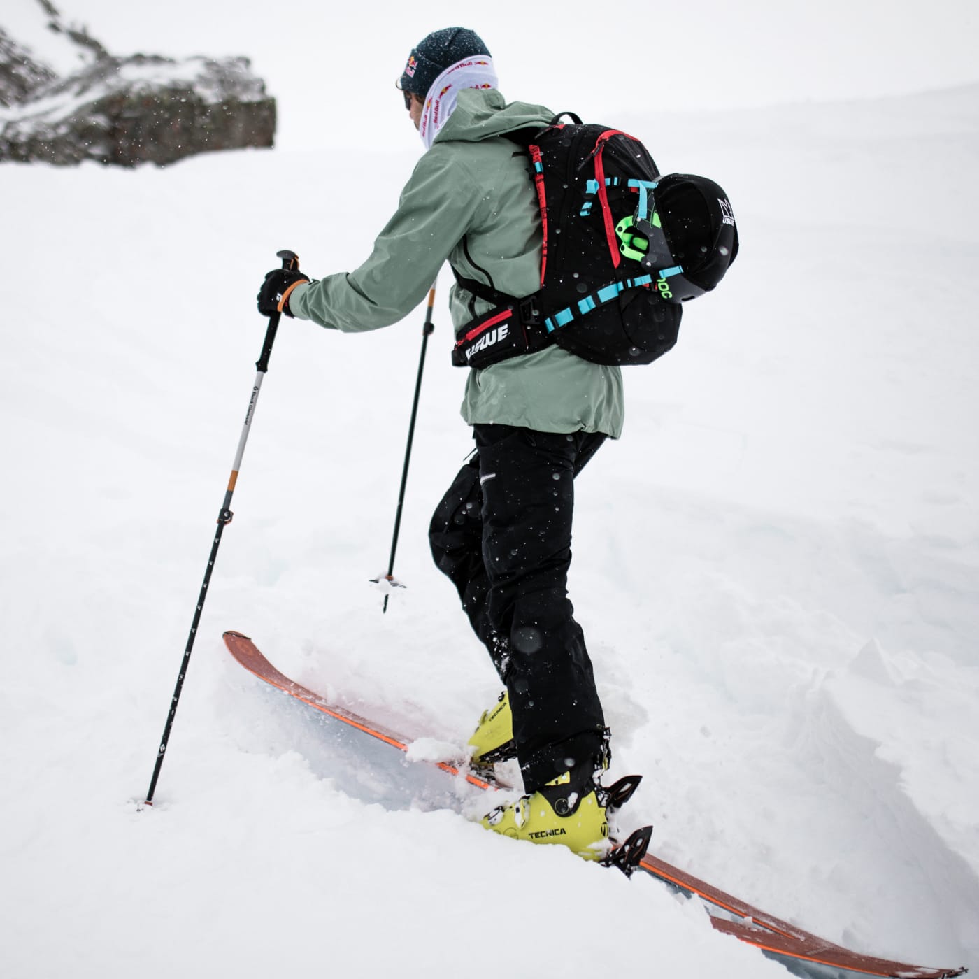 Backcountry skier ascending through deep snow wearing a USWE hydration pack, ski touring uphill in a snowy alpine environment