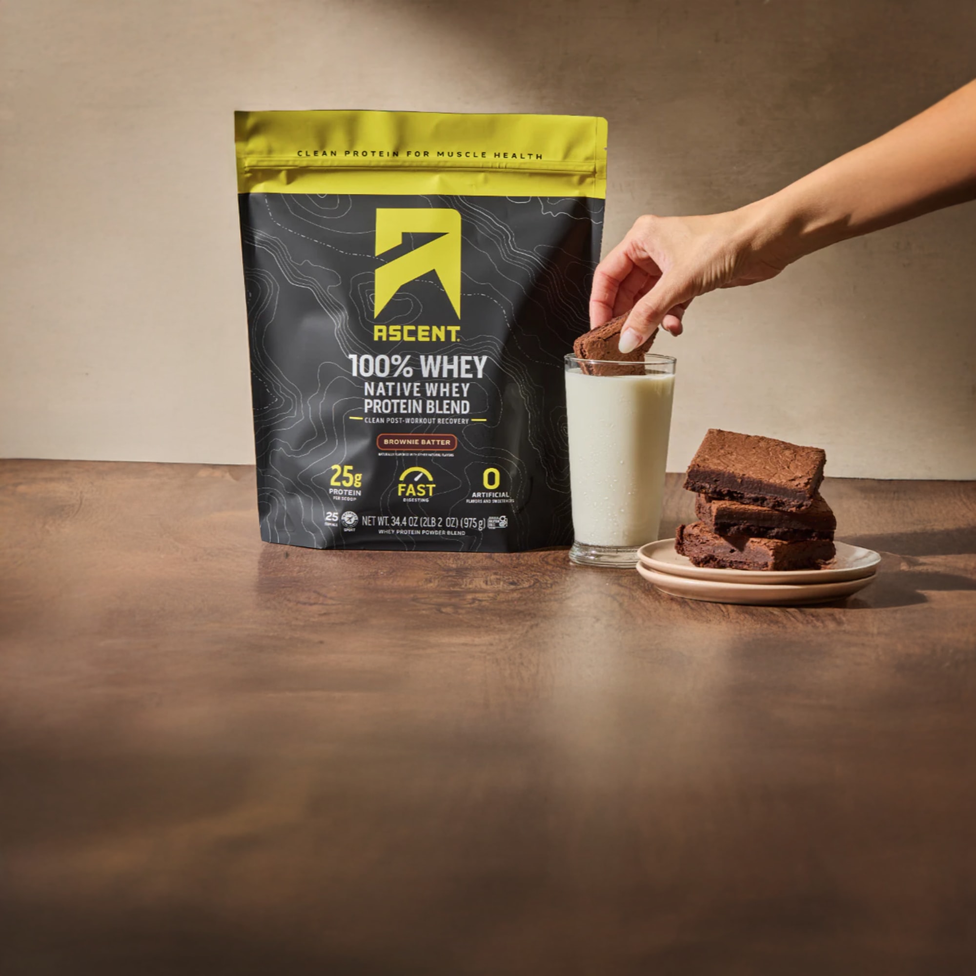 Ascent 100 percent whey protein powder with glass of milk and chocolate brownies for post-training recovery