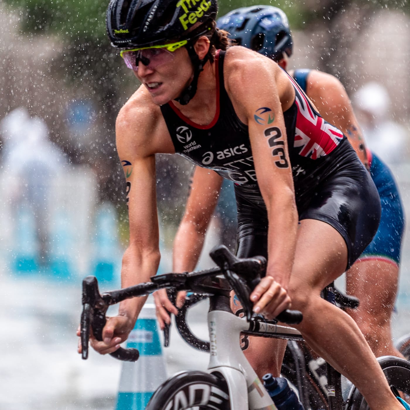 Beth Potter competing in a triathlon, cycling in the rain with The Feed helmet and Team Great Britain race suit, showcasing determination and endurance during competition.