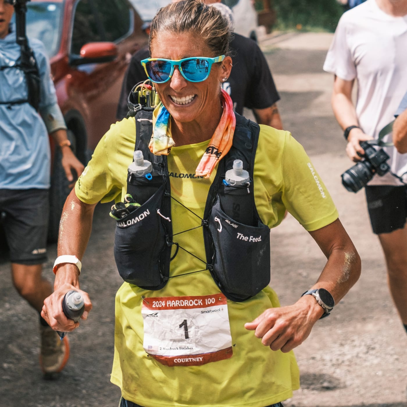 Courtney Dauwalter smiling mid-race at the 2024 Hardrock 100, wearing Salomon gear and The Feed hydration vest, showcasing elite ultrarunning endurance and positive energy during the iconic mountain ultra.”
